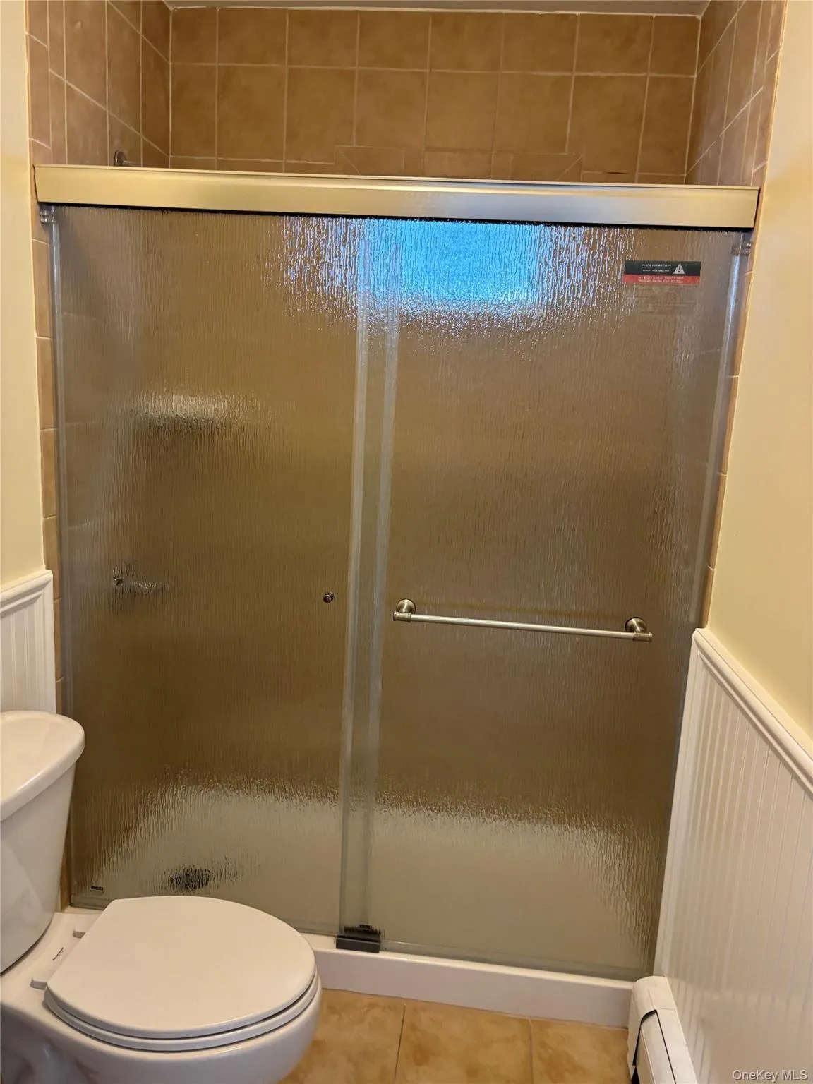 Full bathroom with a stall shower, wainscoting, tile patterned floors, and baseboard heating Full bathroom with a stall shower, wainscoting, tile patterned floors, and baseboard heating