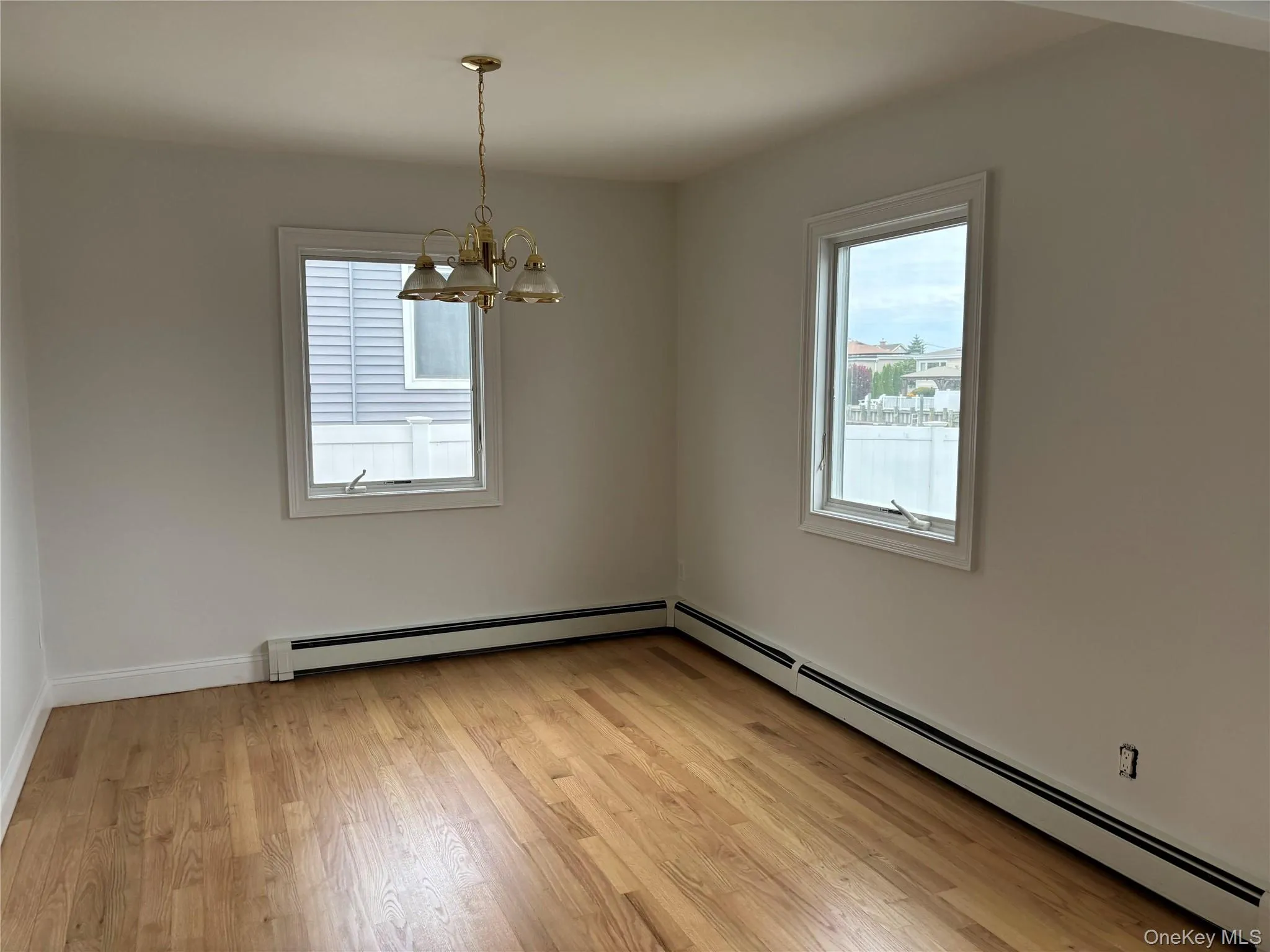 Empty room featuring baseboard heating, light wood-style flooring, and a chandelier Empty room featuring baseboard heating, light wood-style flooring, and a chandelier