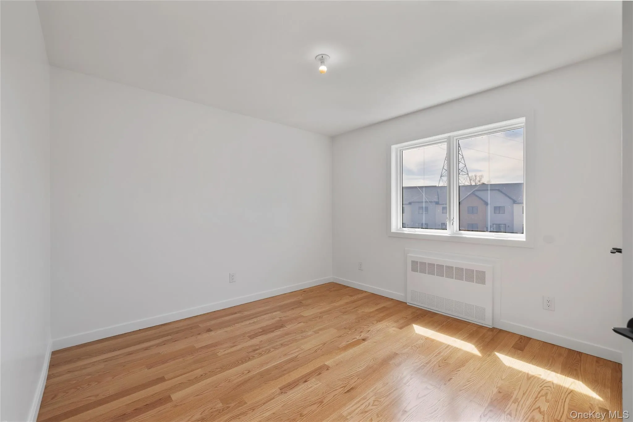 Empty room with radiator heating unit, baseboards, and light wood-style flooring Empty room with radiator heating unit, baseboards, and light wood-style flooring