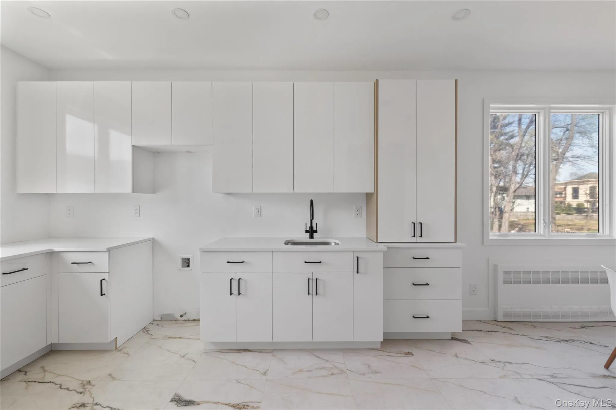 Kitchen featuring white cabinets, a sink, radiator heating unit, marble finish floor, and light countertops Kitchen featuring white cabinets, a sink, radiator heating unit, marble finish floor, and light countertops