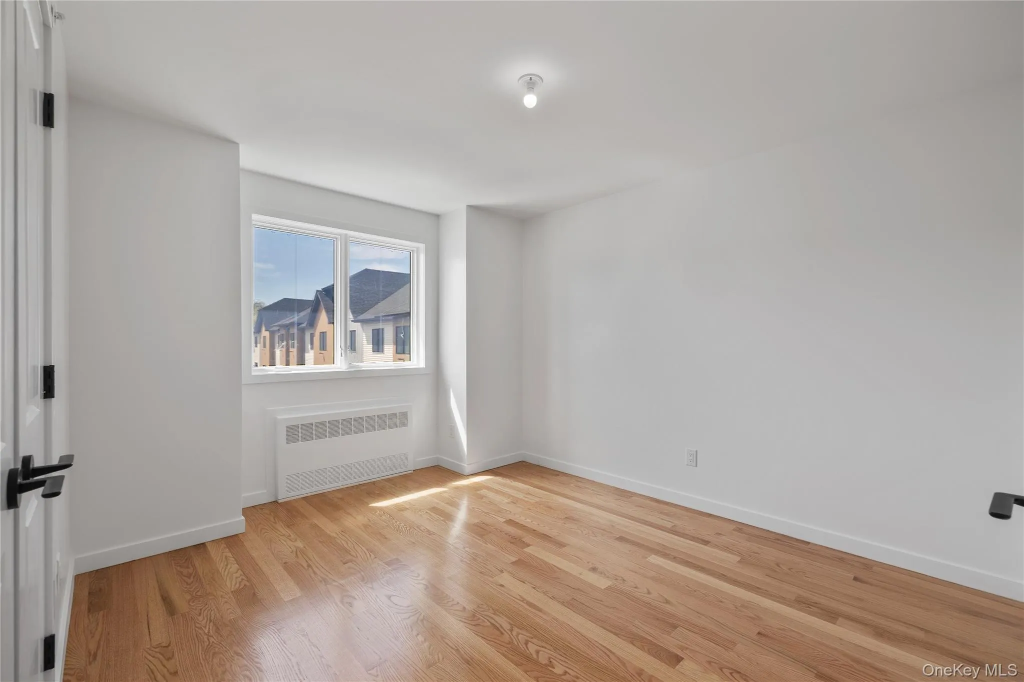 Spare room featuring radiator heating unit, baseboards, and light wood-type flooring Spare room featuring radiator heating unit, baseboards, and light wood-type flooring
