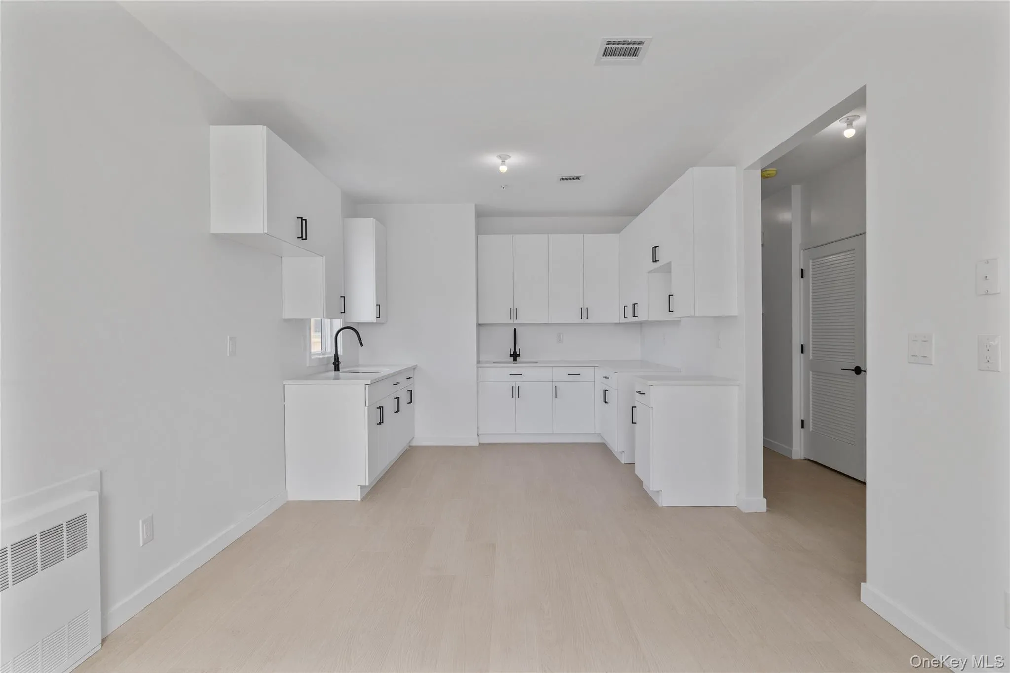 Kitchen with radiator heating unit, light wood finished floors, a sink, and visible vents Kitchen with radiator heating unit, light wood finished floors, a sink, and visible vents