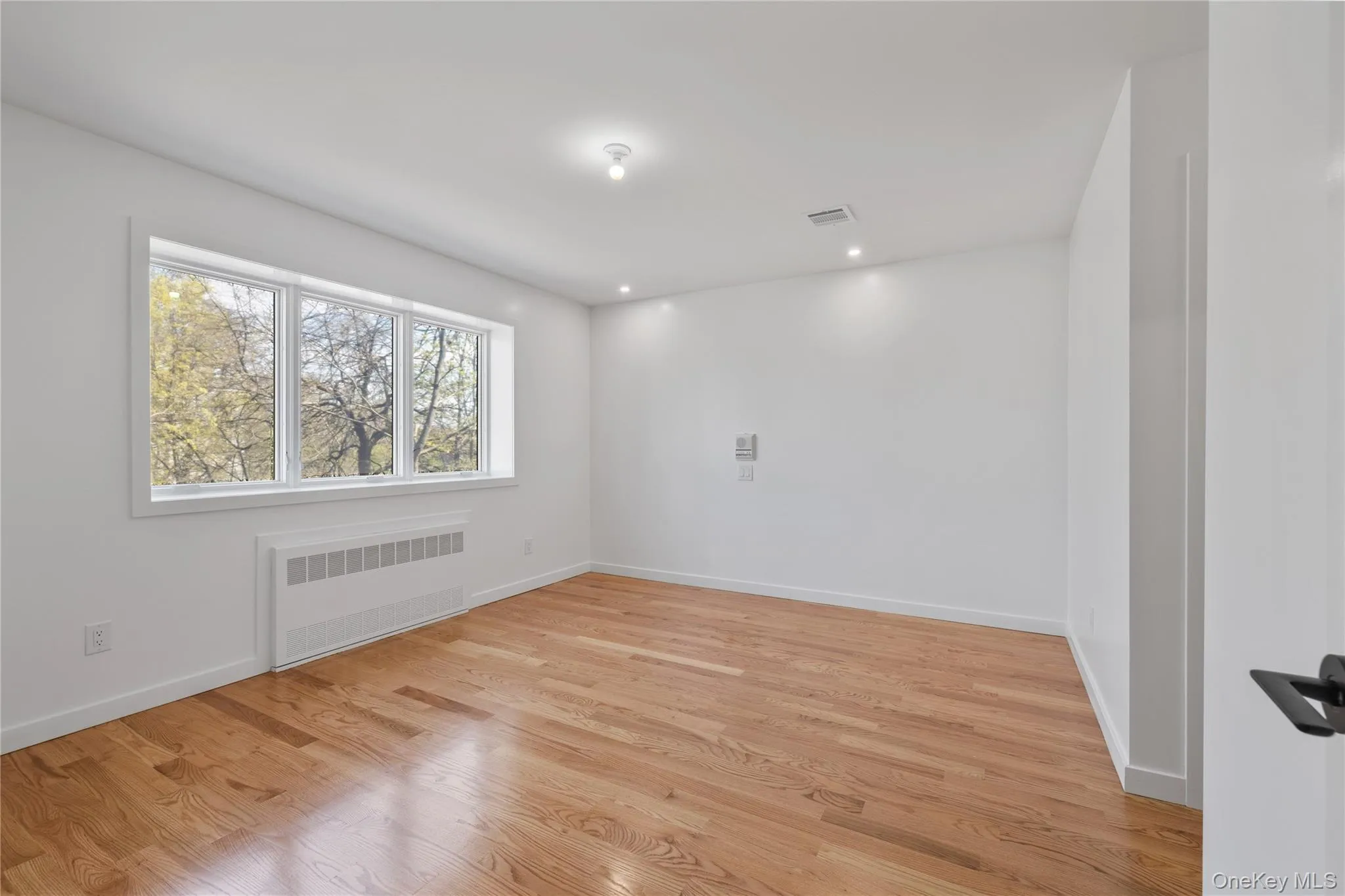 Spare room featuring radiator, light wood-style floors, visible vents, and baseboards Spare room featuring radiator, light wood-style floors, visible vents, and baseboards