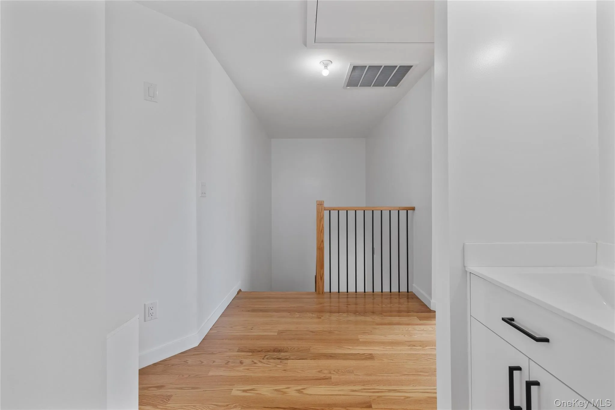 Hallway featuring visible vents, a sink, an upstairs landing, light wood-style floors, and baseboards Hallway featuring visible vents, a sink, an upstairs landing, light wood-style floors, and baseboards