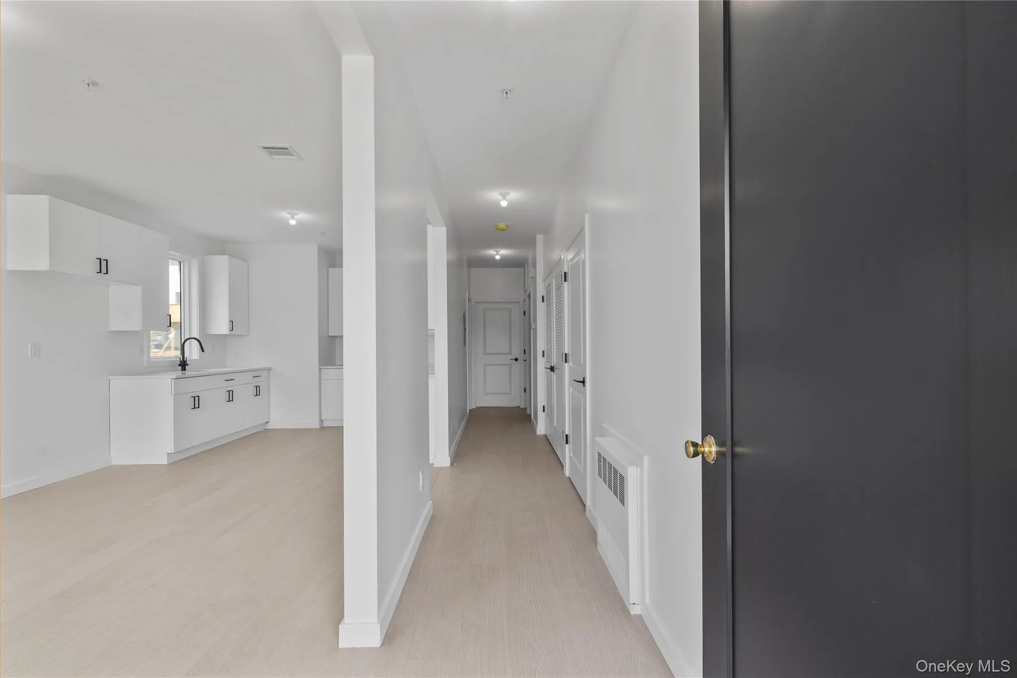 Corridor featuring light wood-style flooring, visible vents, baseboards, and a sink Corridor featuring light wood-style flooring, visible vents, baseboards, and a sink