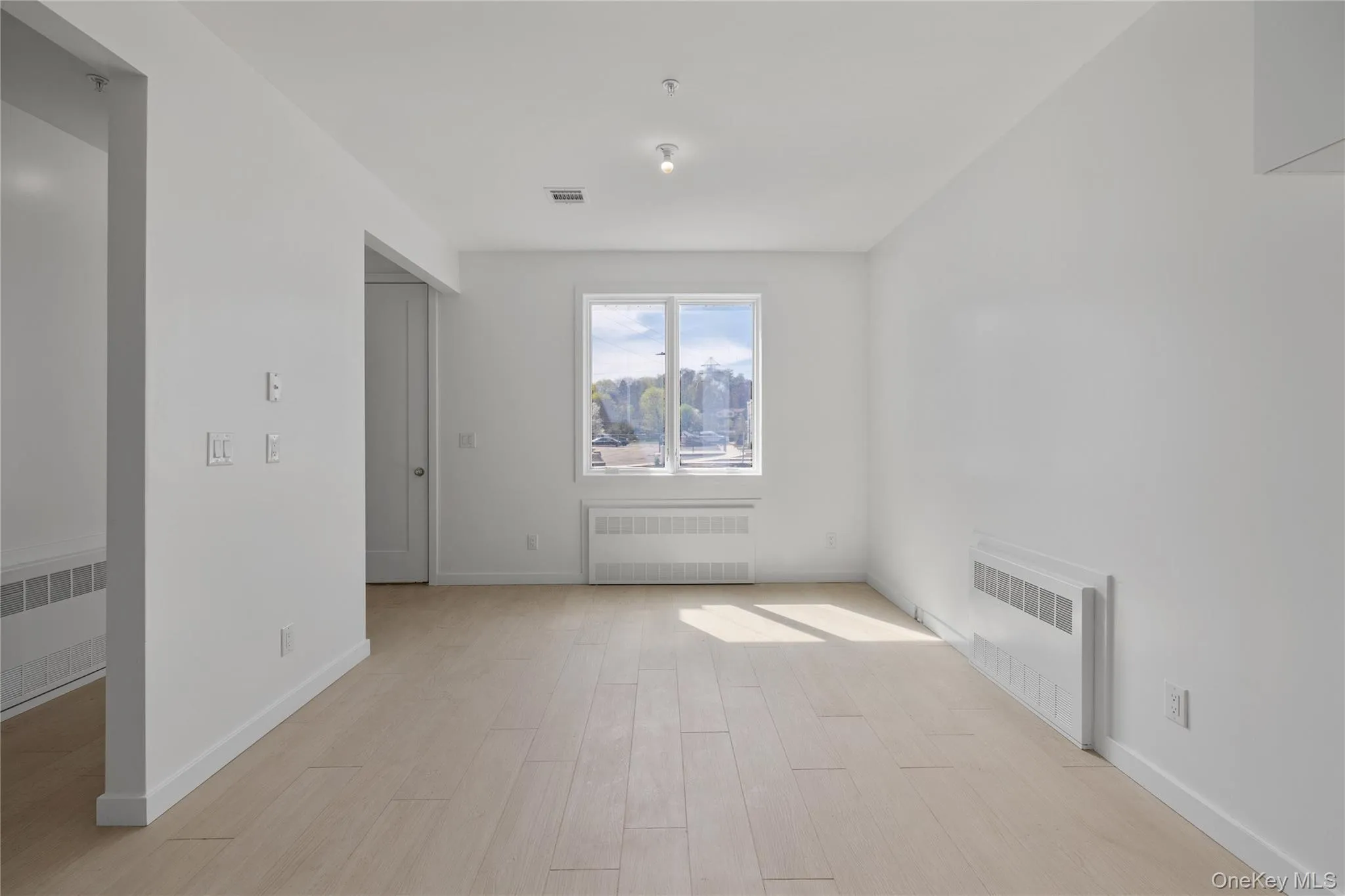 Spare room with baseboards, radiator heating unit, visible vents, and light wood-type flooring Spare room with baseboards, radiator heating unit, visible vents, and light wood-type flooring