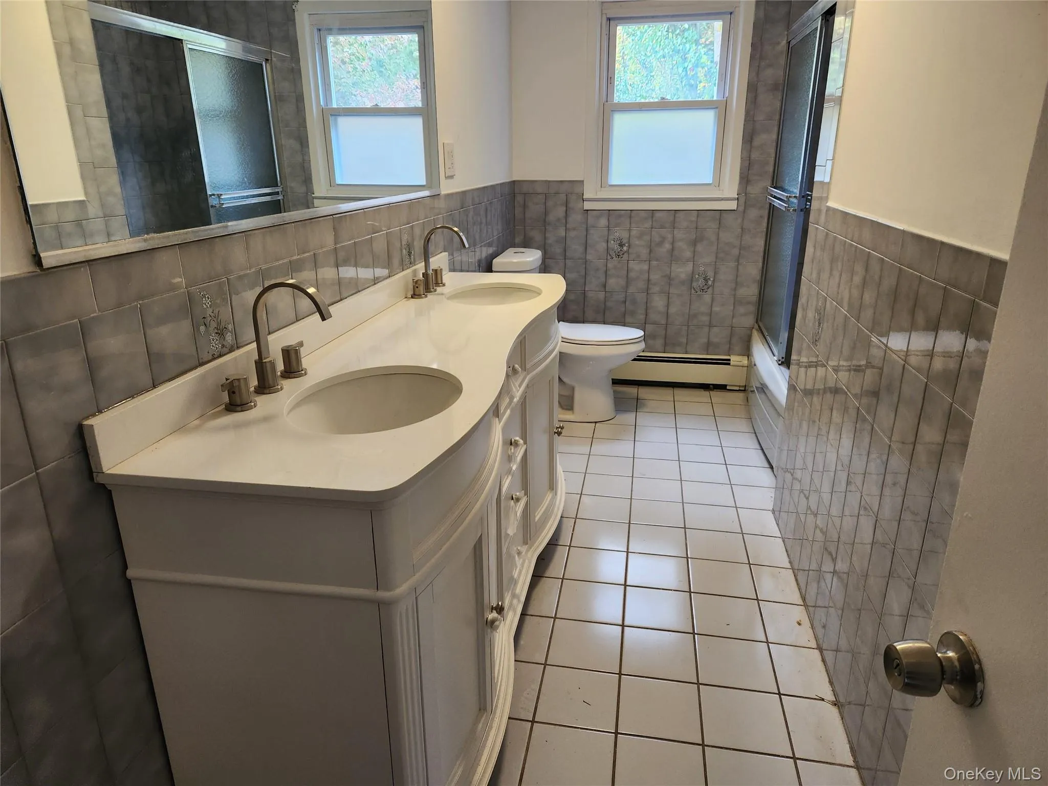 Full bathroom featuring light tile patterned flooring, tile walls, a shower with door, double vanity, and plenty of natural light Full bathroom featuring light tile patterned flooring, tile walls, a shower with door, double vanity, and plenty of natural light