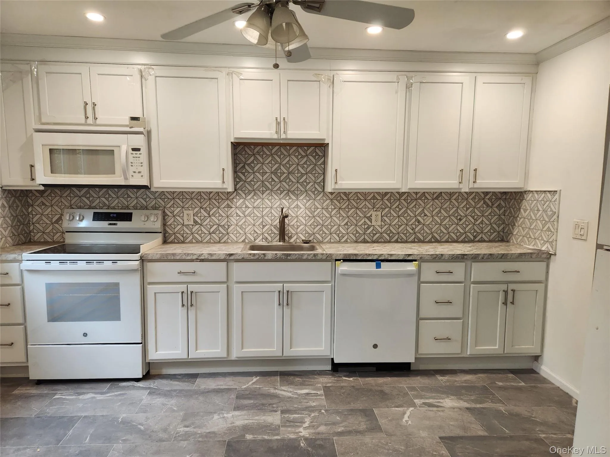 Kitchen featuring white appliances, backsplash, ceiling fan, white cabinetry, and recessed lighting Kitchen featuring white appliances, backsplash, ceiling fan, white cabinetry, and recessed lighting
