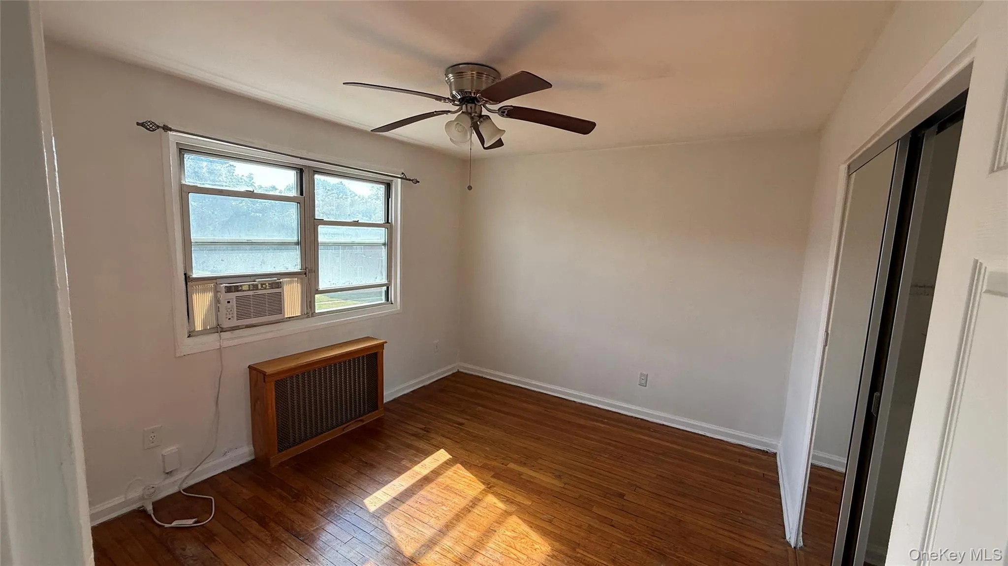 Spare room with dark wood-type flooring, radiator, a ceiling fan, and cooling unit Spare room with dark wood-type flooring, radiator, a ceiling fan, and cooling unit
