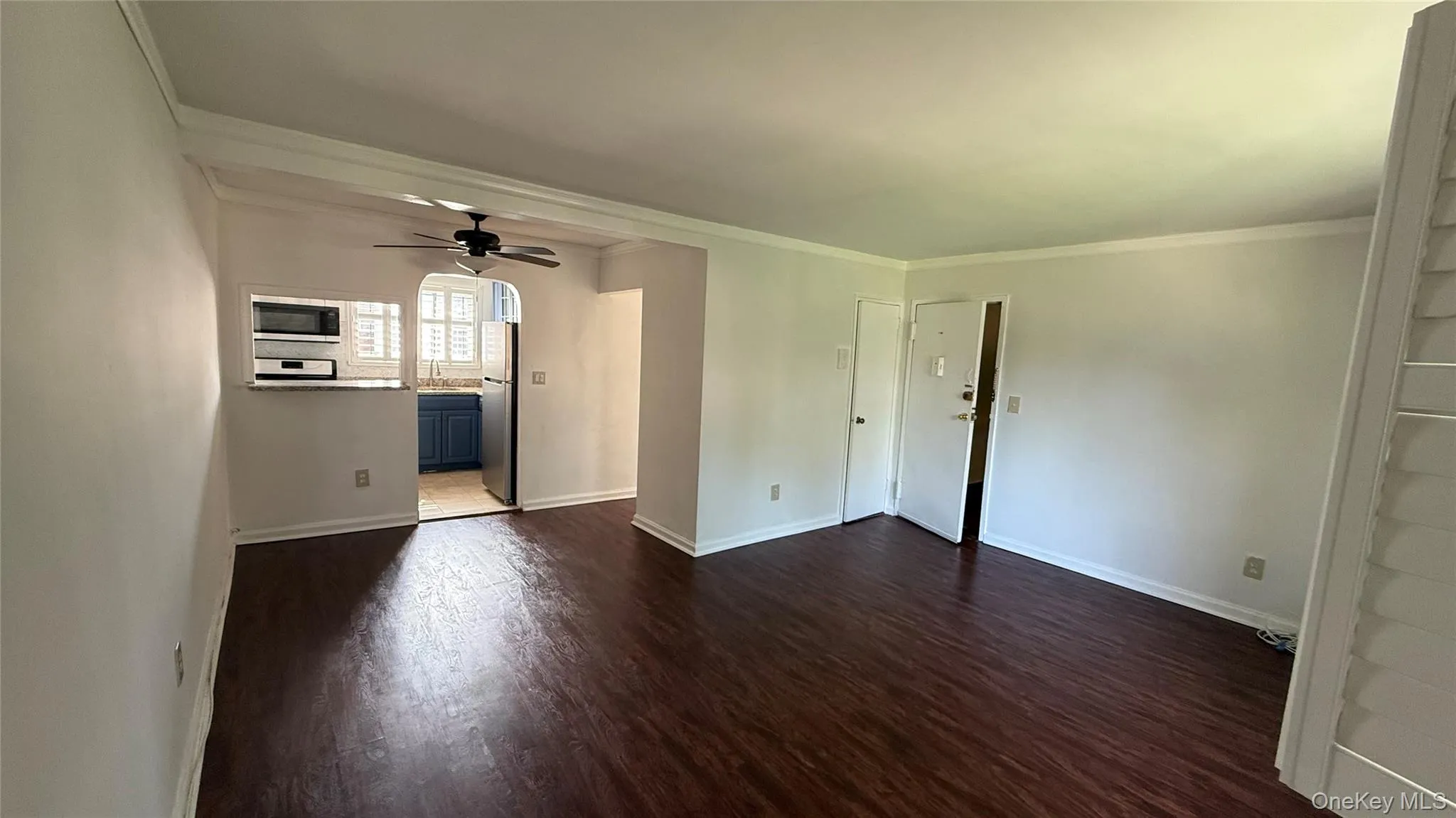 Unfurnished living room featuring ornamental molding, dark wood-type flooring, and a ceiling fan Unfurnished living room featuring ornamental molding, dark wood-type flooring, and a ceiling fan