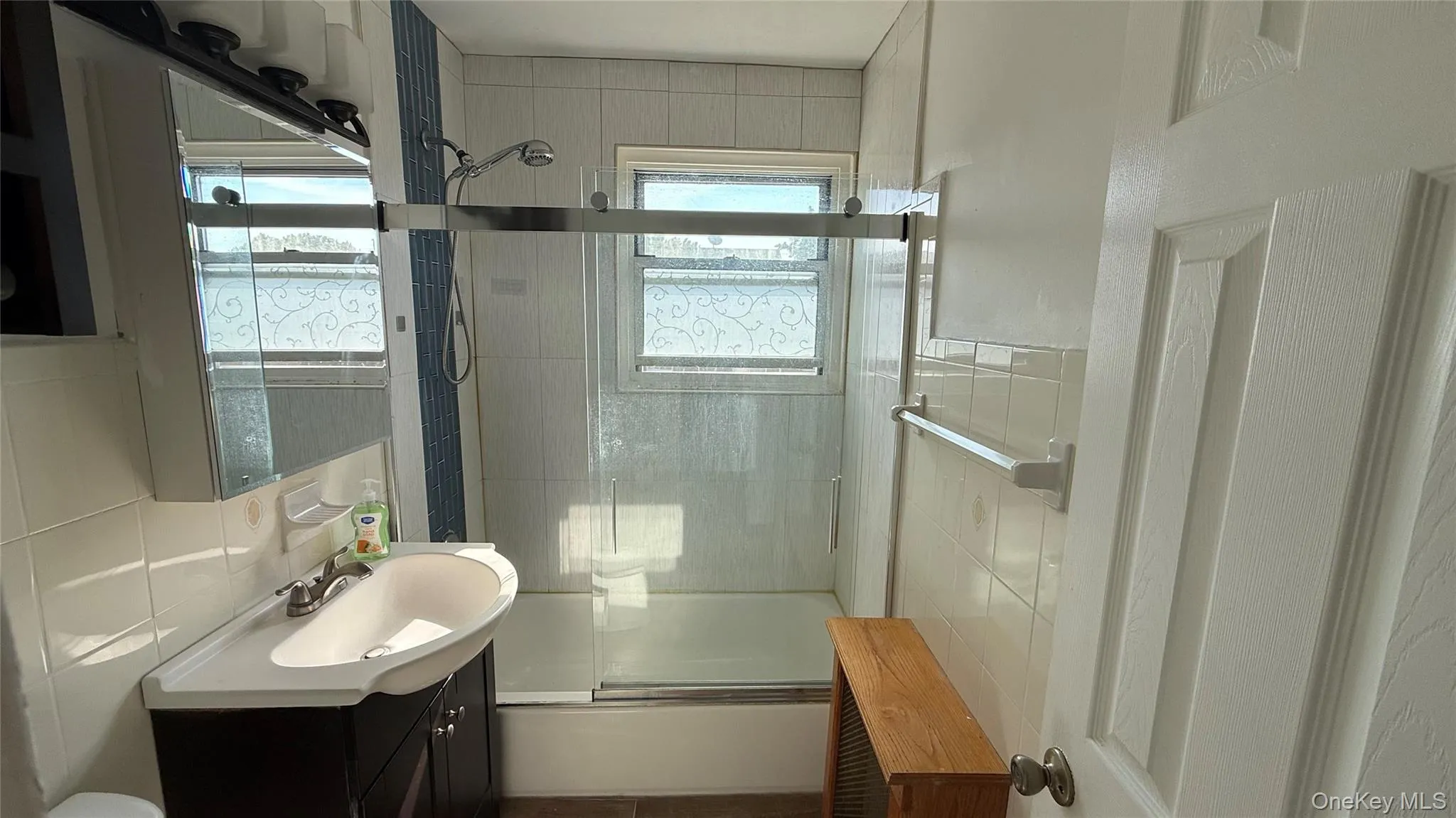 Full bathroom with bath / shower combo with glass door, vanity, and tile walls Full bathroom with bath / shower combo with glass door, vanity, and tile walls