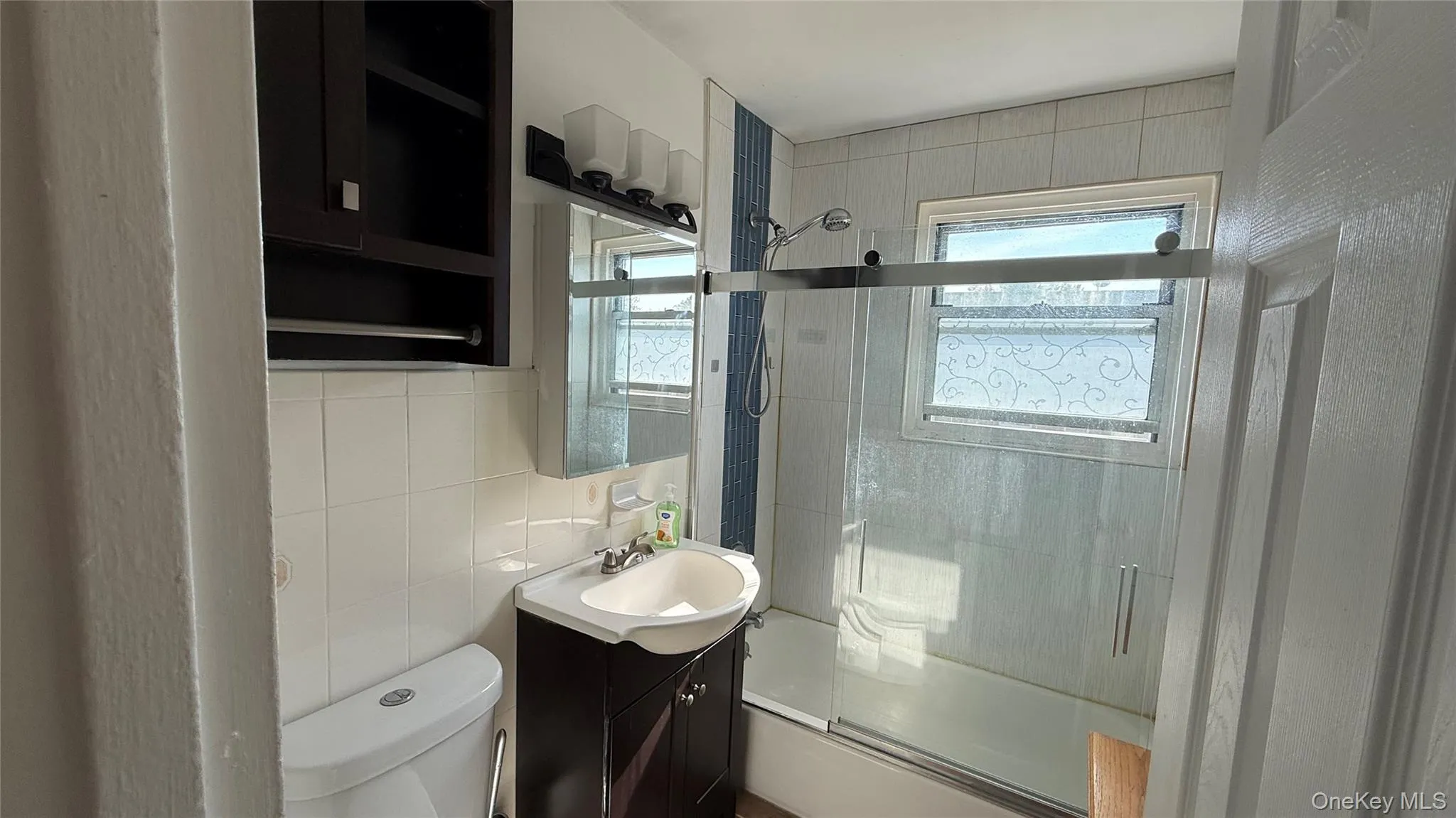 Bathroom featuring bath / shower combo with glass door, tile walls, vanity, and tasteful backsplash Bathroom featuring bath / shower combo with glass door, tile walls, vanity, and tasteful backsplash
