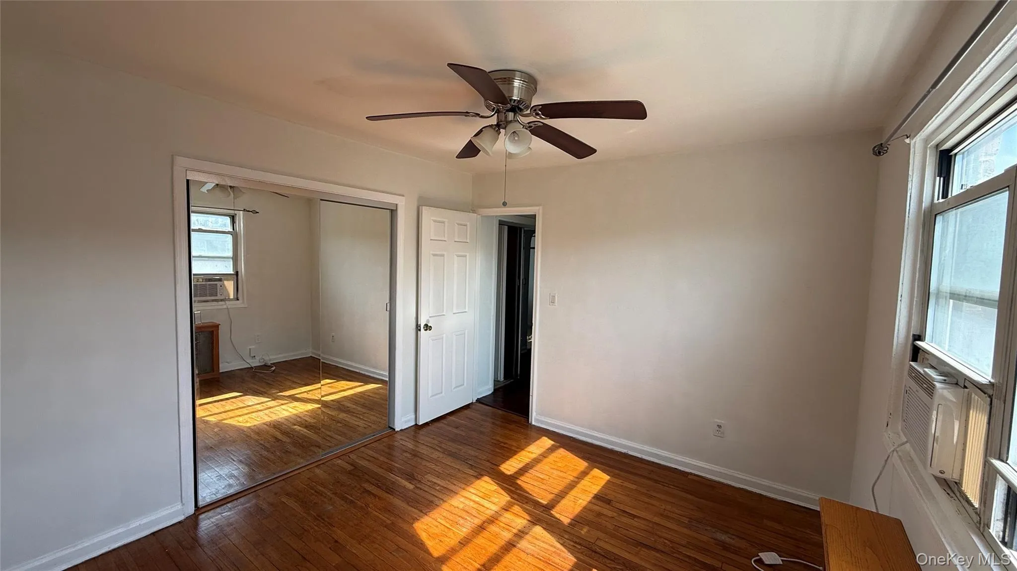 Unfurnished bedroom featuring wood-type flooring, a closet, a ceiling fan, and cooling unit Unfurnished bedroom featuring wood-type flooring, a closet, a ceiling fan, and cooling unit