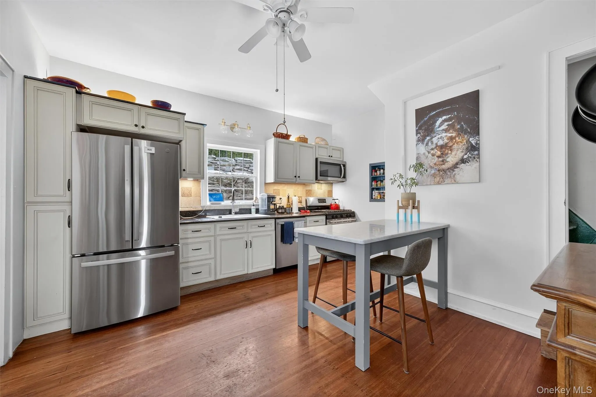 Kitchen featuring stainless steel appliances, backsplash, dark wood-style floors, a ceiling fan, and dark countertops Kitchen featuring stainless steel appliances, backsplash, dark wood-style floors, a ceiling fan, and dark countertops