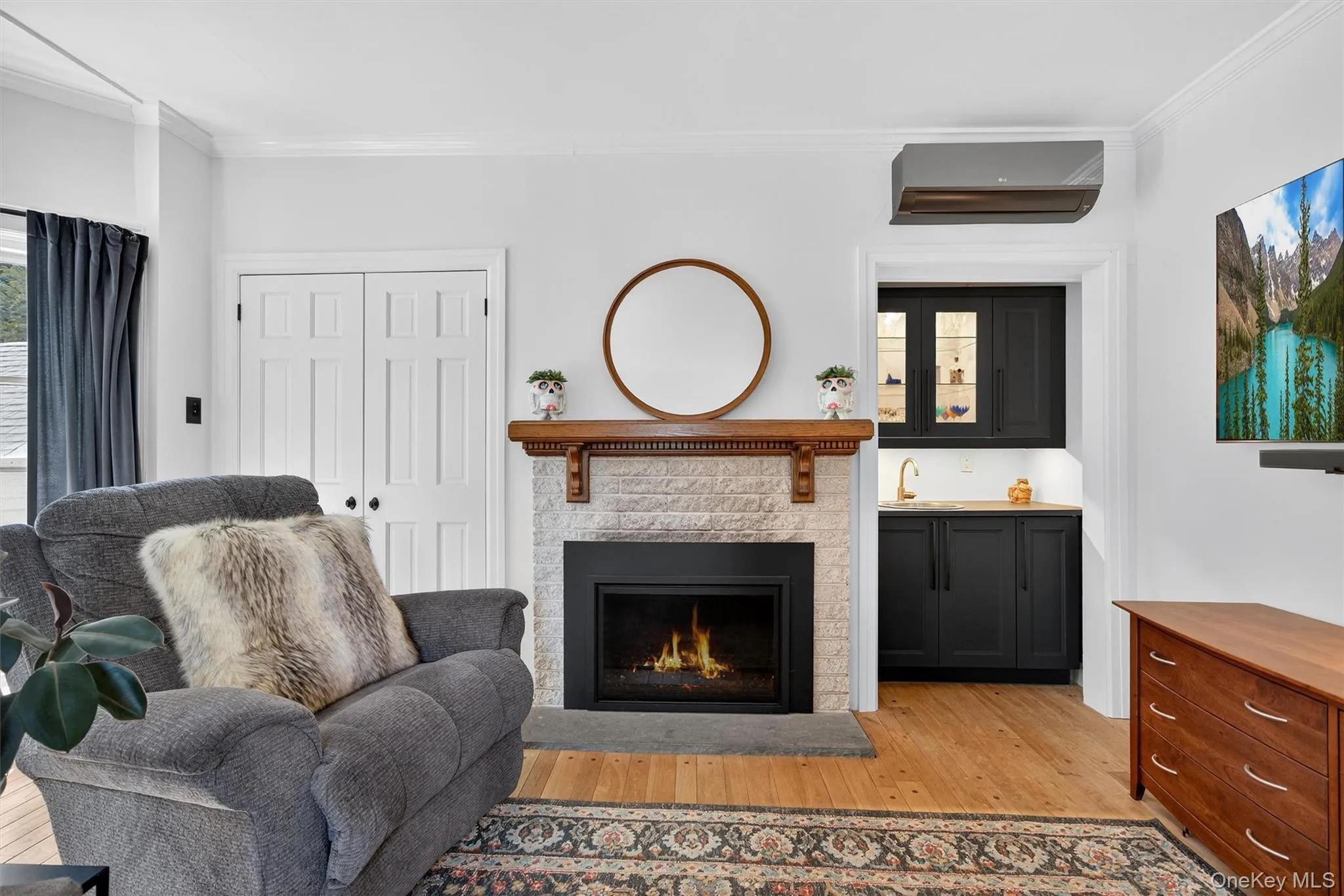 Living room with light wood finished floors, ornamental molding, a wall unit AC, and a brick fireplace Living room with light wood finished floors, ornamental molding, a wall unit AC, and a brick fireplace