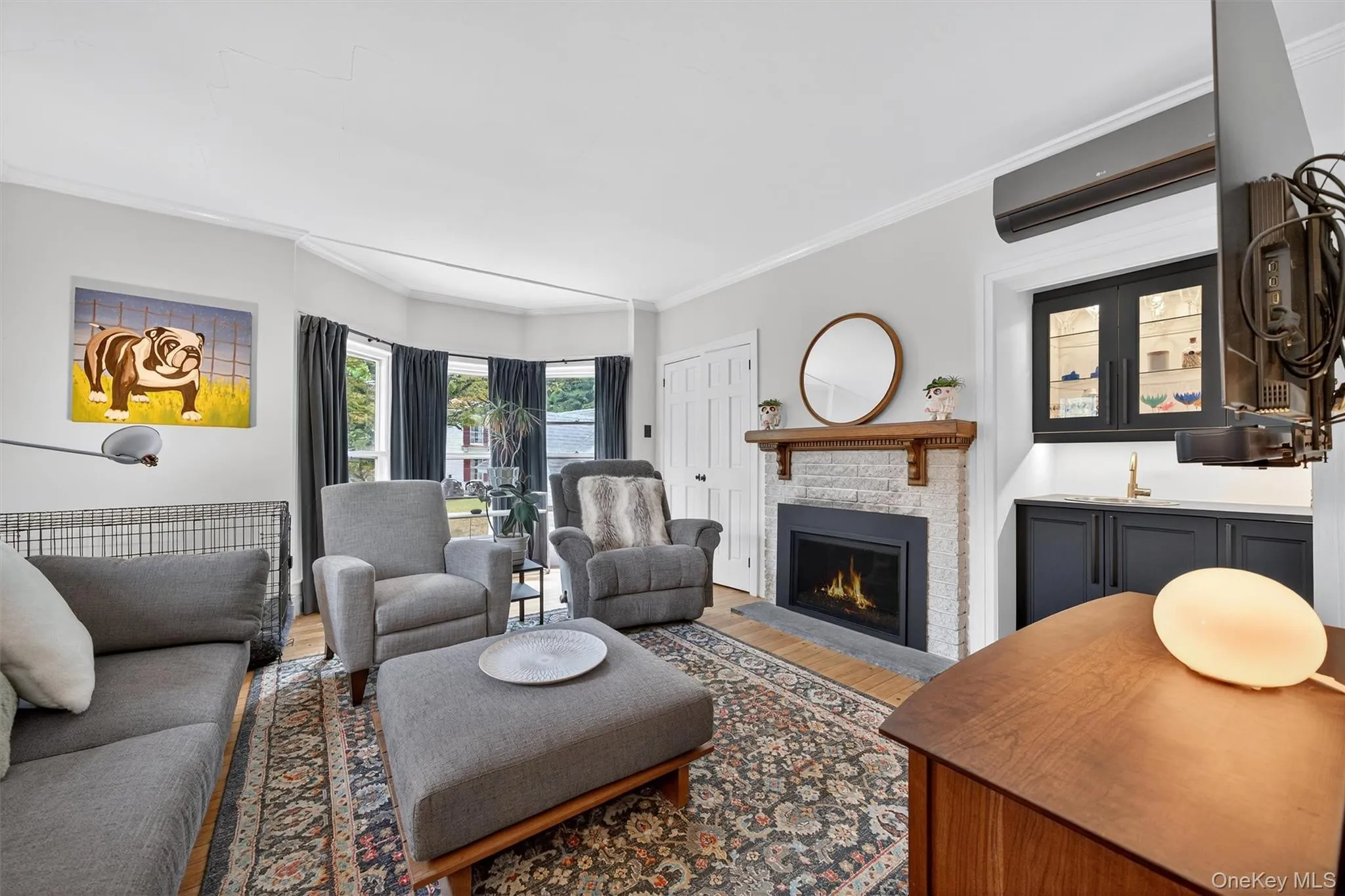Living room featuring ornamental molding, a stone fireplace, wood finished floors, a wall mounted air conditioner, and wet bar Living room featuring ornamental molding, a stone fireplace, wood finished floors, a wall mounted air conditioner, and wet bar