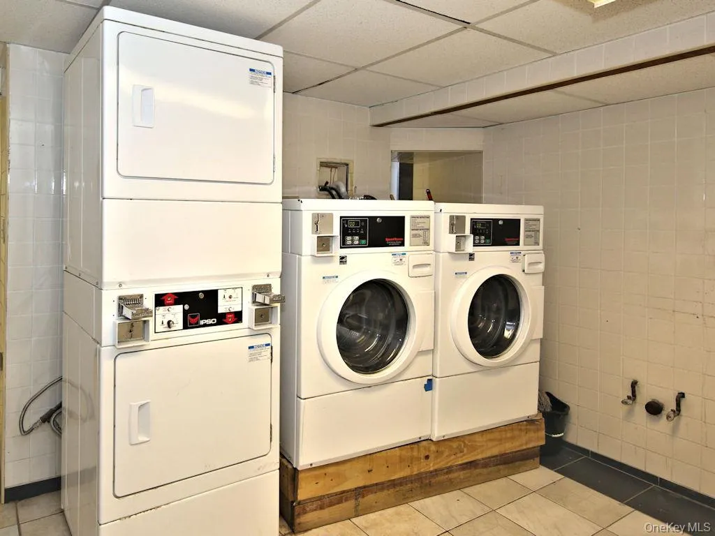 Communal laundry room featuring tile walls, light tile patterned flooring, and stacked washer / dryer Communal laundry room featuring tile walls, light tile patterned flooring, and stacked washer / dryer