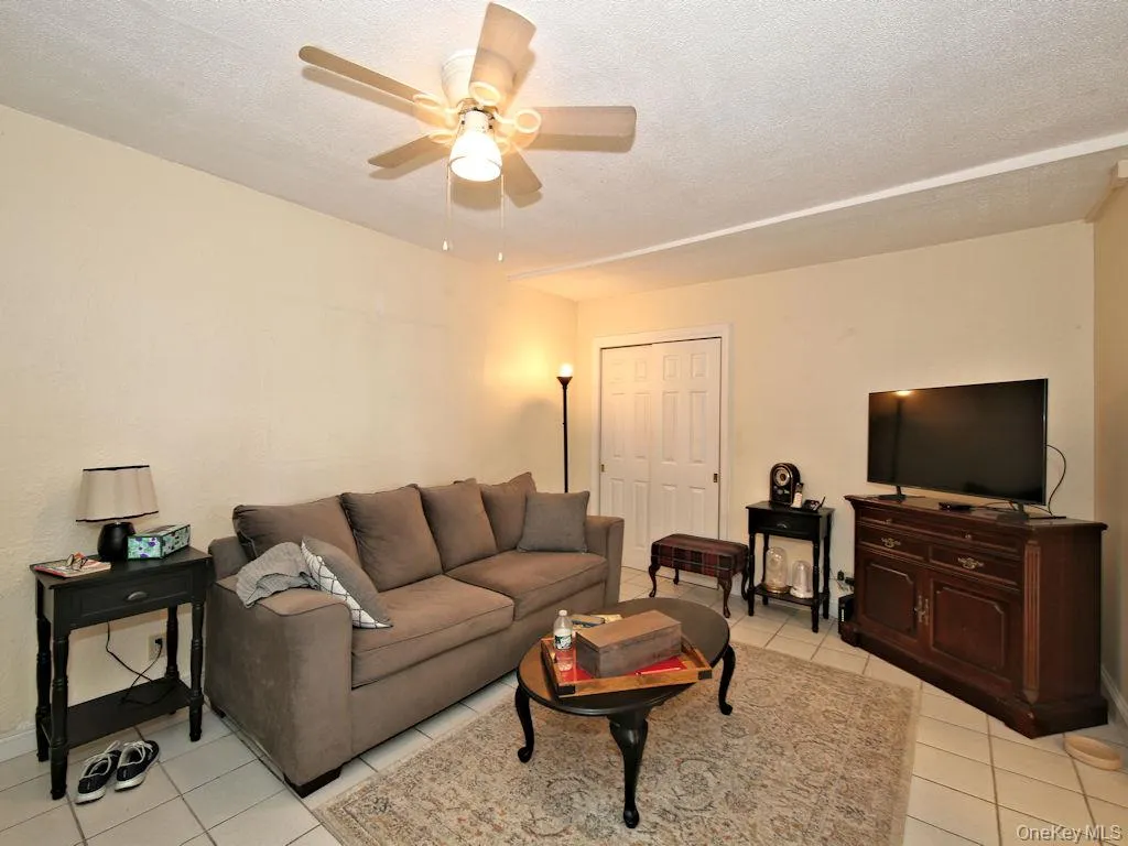 Living area featuring light tile patterned floors, a textured ceiling, and ceiling fan Living area featuring light tile patterned floors, a textured ceiling, and ceiling fan