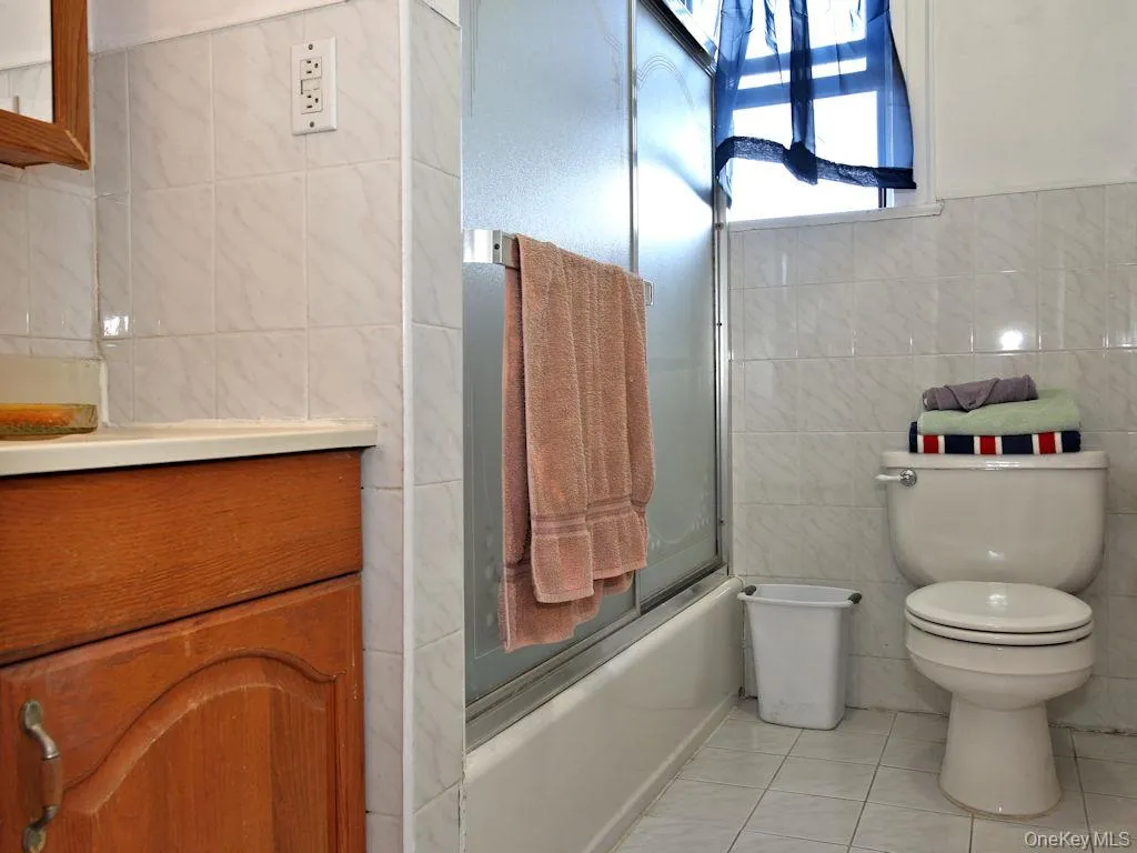 Bathroom with tile walls, enclosed tub / shower combo, tile patterned flooring, and vanity Bathroom with tile walls, enclosed tub / shower combo, tile patterned flooring, and vanity