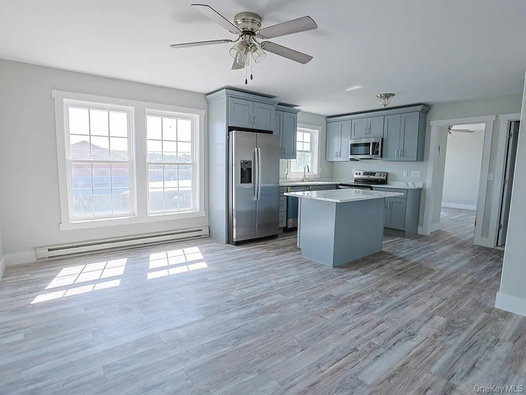 Kitchen with a ceiling fan, appliances with stainless steel finishes, gray cabinetry, a baseboard radiator, and a center island Kitchen with a ceiling fan, appliances with stainless steel finishes, gray cabinetry, a baseboard radiator, and a center island