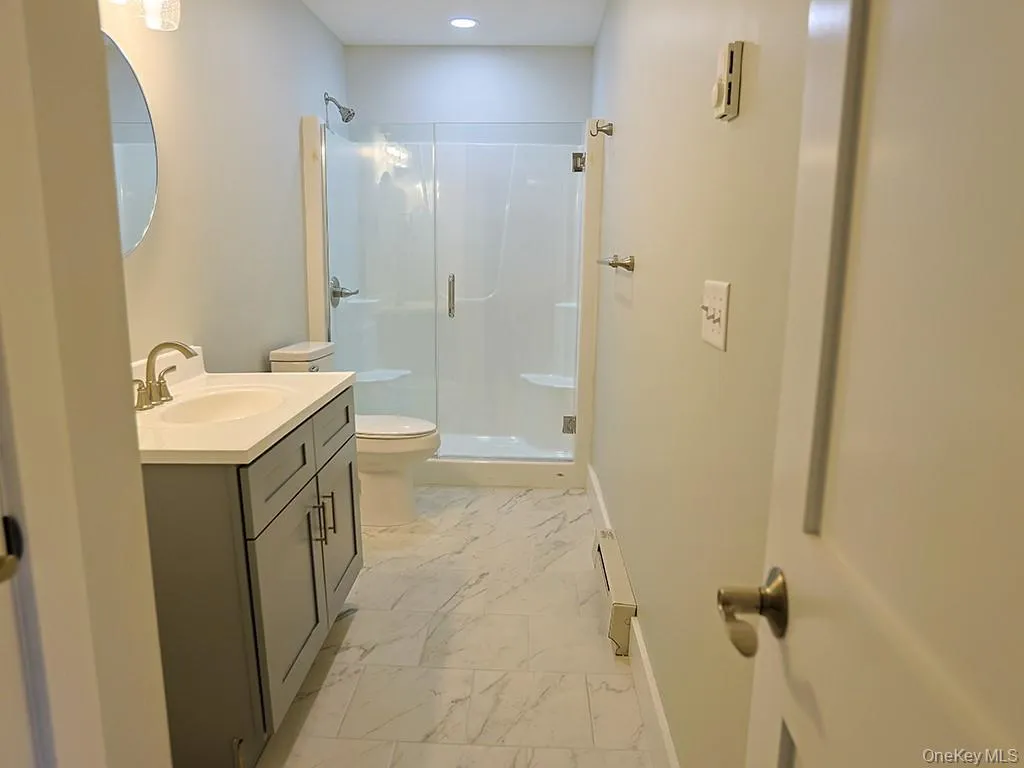 Full bathroom featuring a stall shower, vanity, light marble finish floors, and baseboard heating Full bathroom featuring a stall shower, vanity, light marble finish floors, and baseboard heating