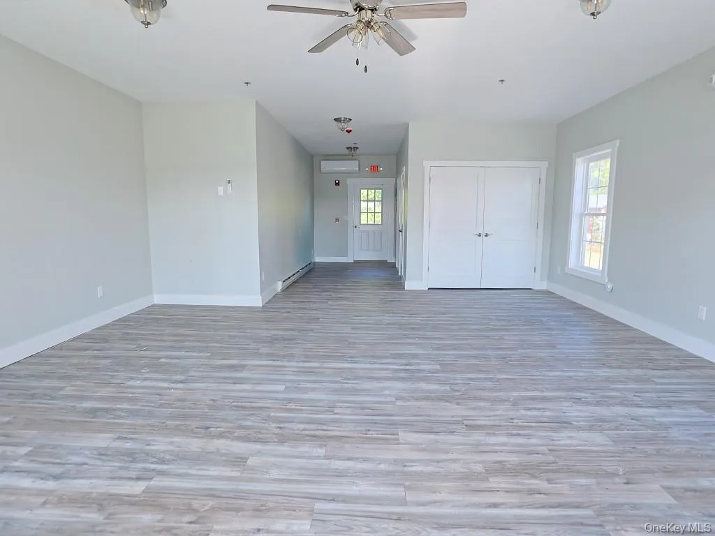 Unfurnished living room with healthy amount of natural light, light wood finished floors, a baseboard heating unit, and a ceiling fan Unfurnished living room with healthy amount of natural light, light wood finished floors, a baseboard heating unit, and a ceiling fan