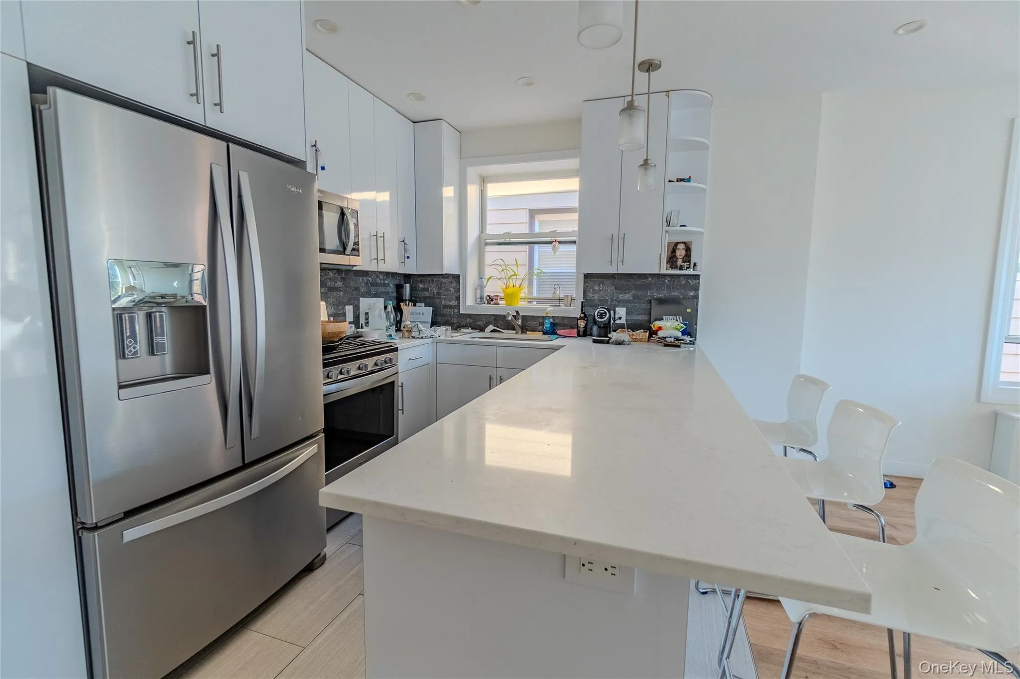 Kitchen with stainless steel appliances, a peninsula, a kitchen bar, decorative light fixtures, and light stone counters Kitchen with stainless steel appliances, a peninsula, a kitchen bar, decorative light fixtures, and light stone counters