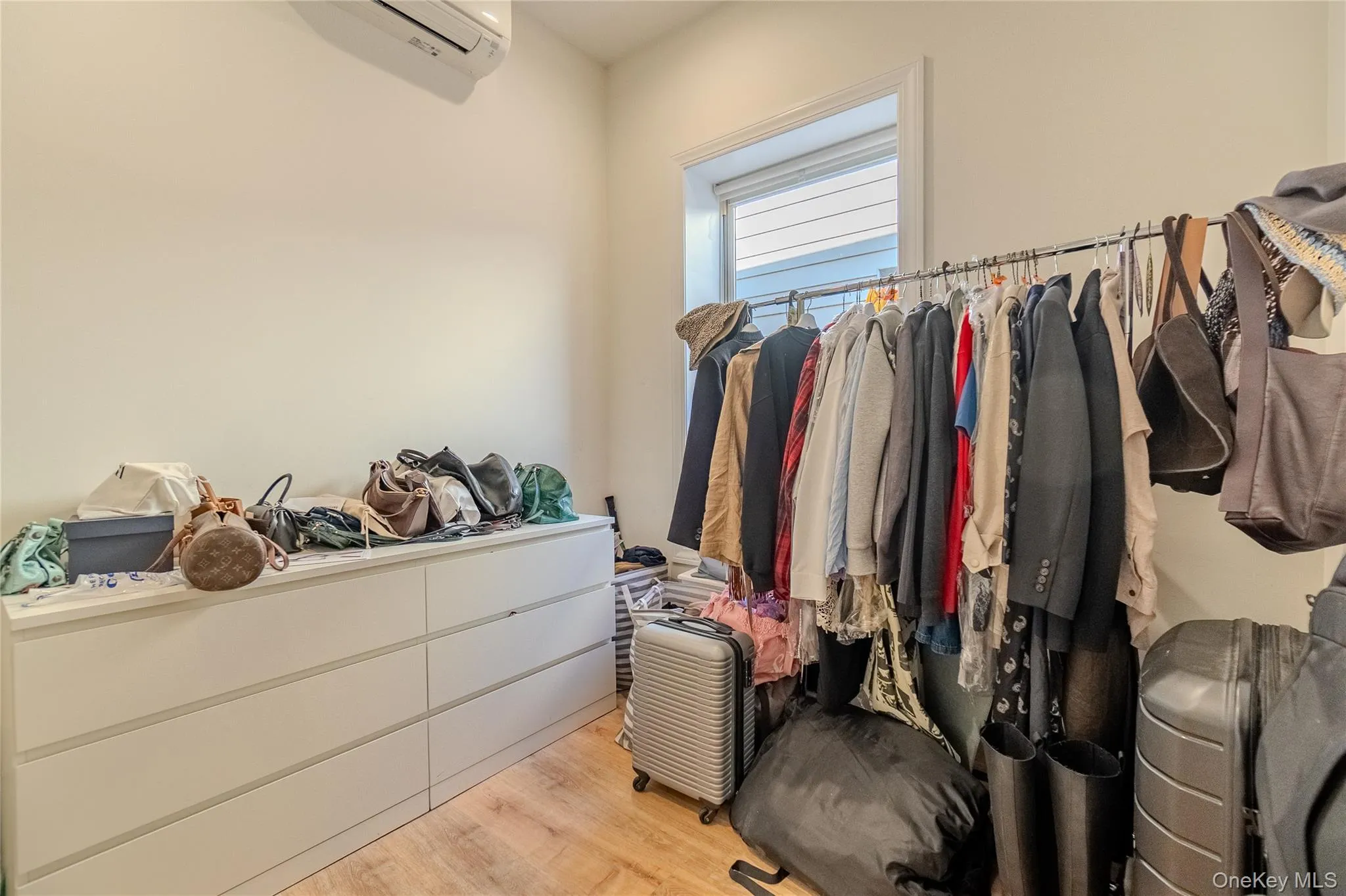 Walk in closet with light wood finished floors and an AC wall unit Walk in closet with light wood finished floors and an AC wall unit