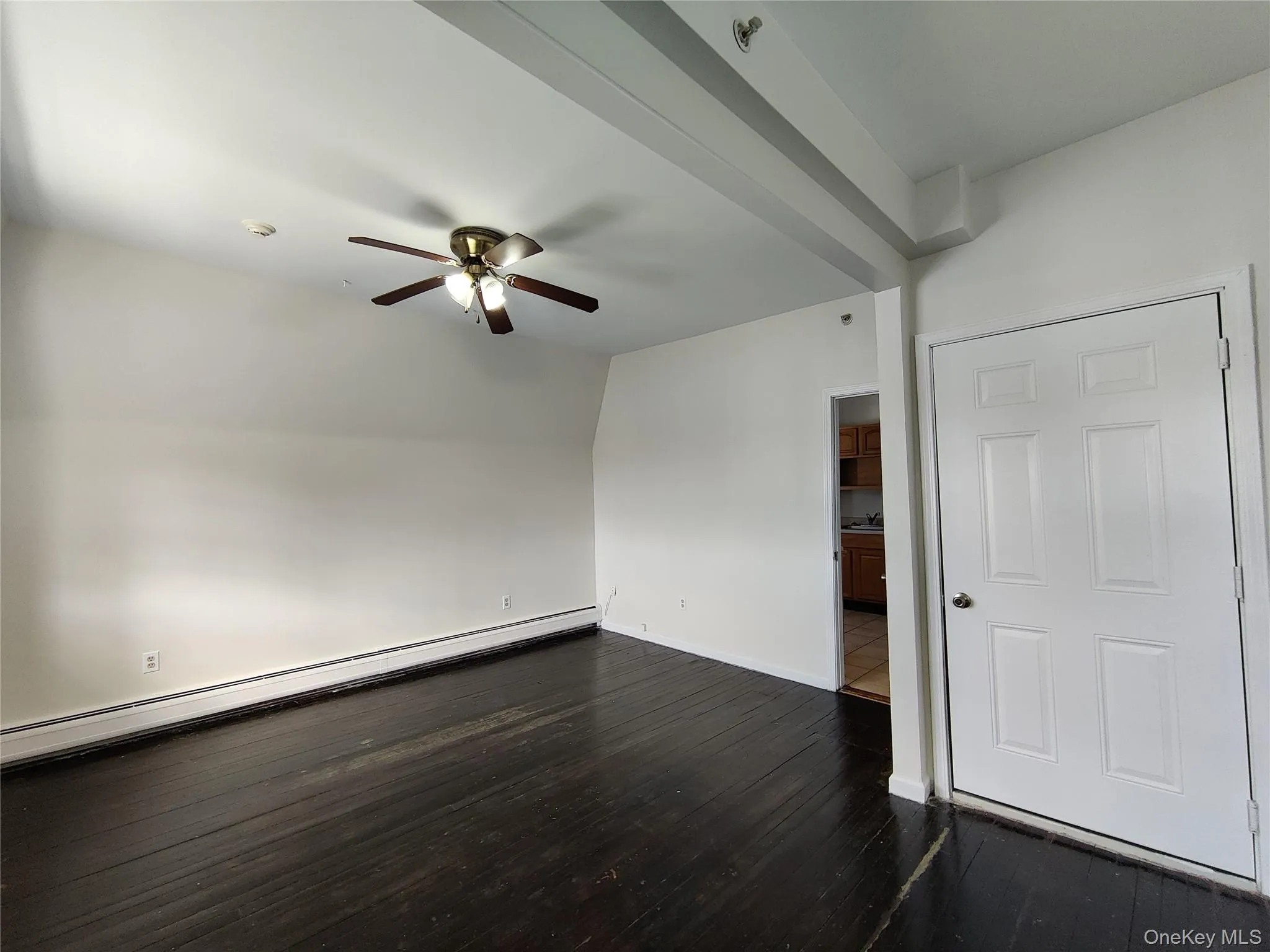 Spare room featuring baseboard heating, dark wood-style flooring, and ceiling fan Spare room featuring baseboard heating, dark wood-style flooring, and ceiling fan