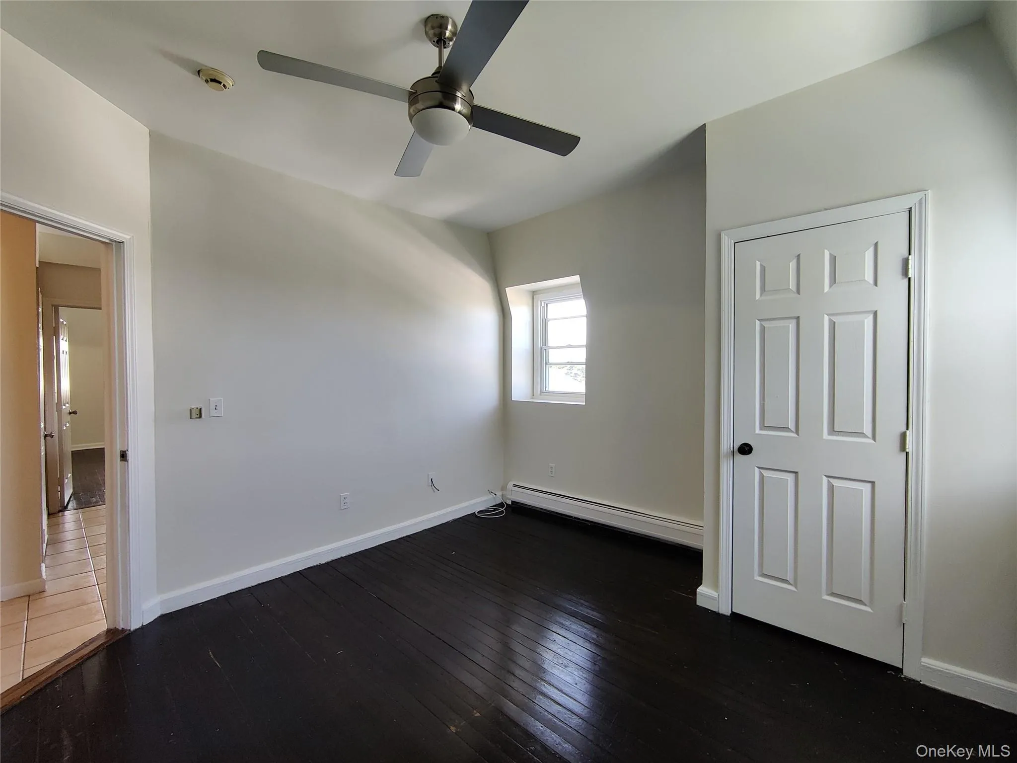 Unfurnished bedroom featuring baseboard heating, dark wood-style flooring, and a ceiling fan Unfurnished bedroom featuring baseboard heating, dark wood-style flooring, and a ceiling fan
