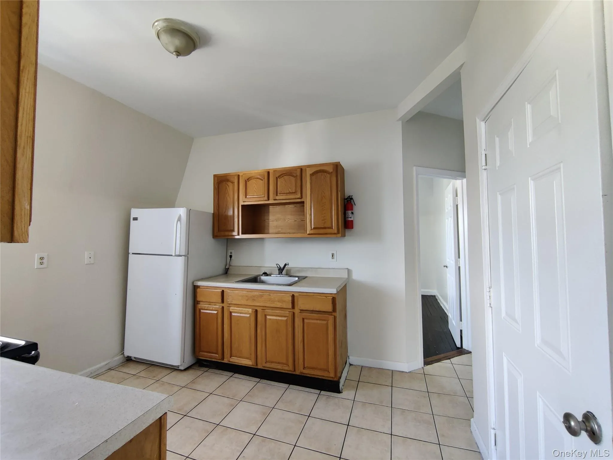 Kitchen with brown cabinets, freestanding refrigerator, light tile patterned flooring, and light countertops Kitchen with brown cabinets, freestanding refrigerator, light tile patterned flooring, and light countertops