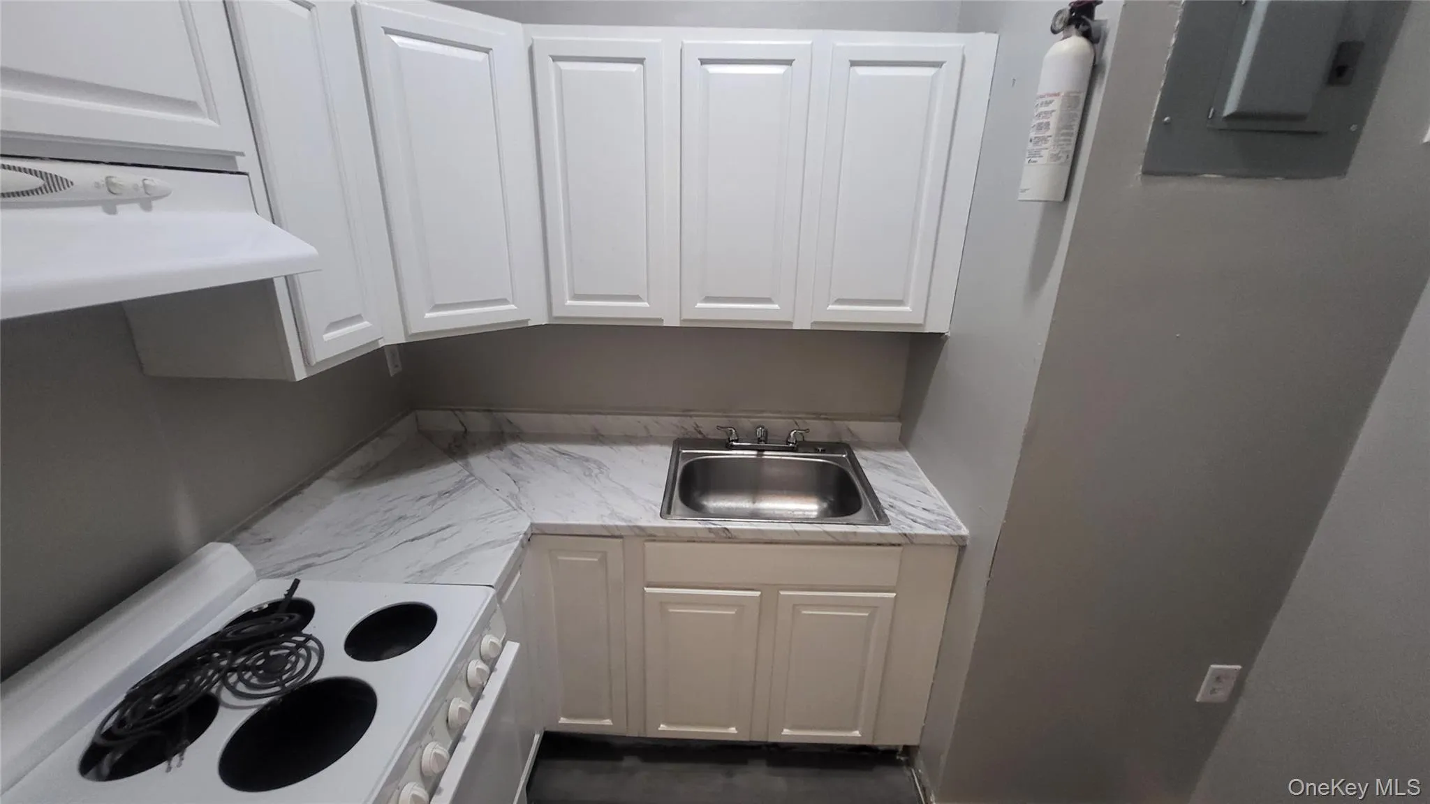 Kitchen featuring white electric stove, light countertops, ventilation hood, white cabinetry, and electric panel Kitchen featuring white electric stove, light countertops, ventilation hood, white cabinetry, and electric panel