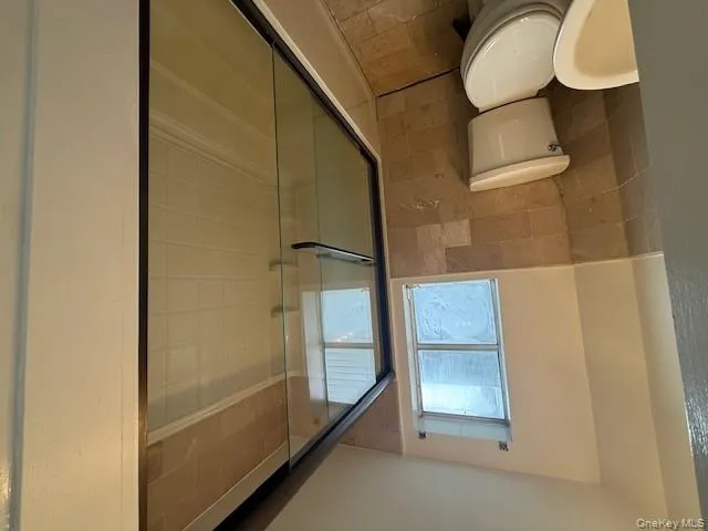 Bathroom with tile walls, bath / shower combo with glass door, and a wainscoted wall Bathroom with tile walls, bath / shower combo with glass door, and a wainscoted wall