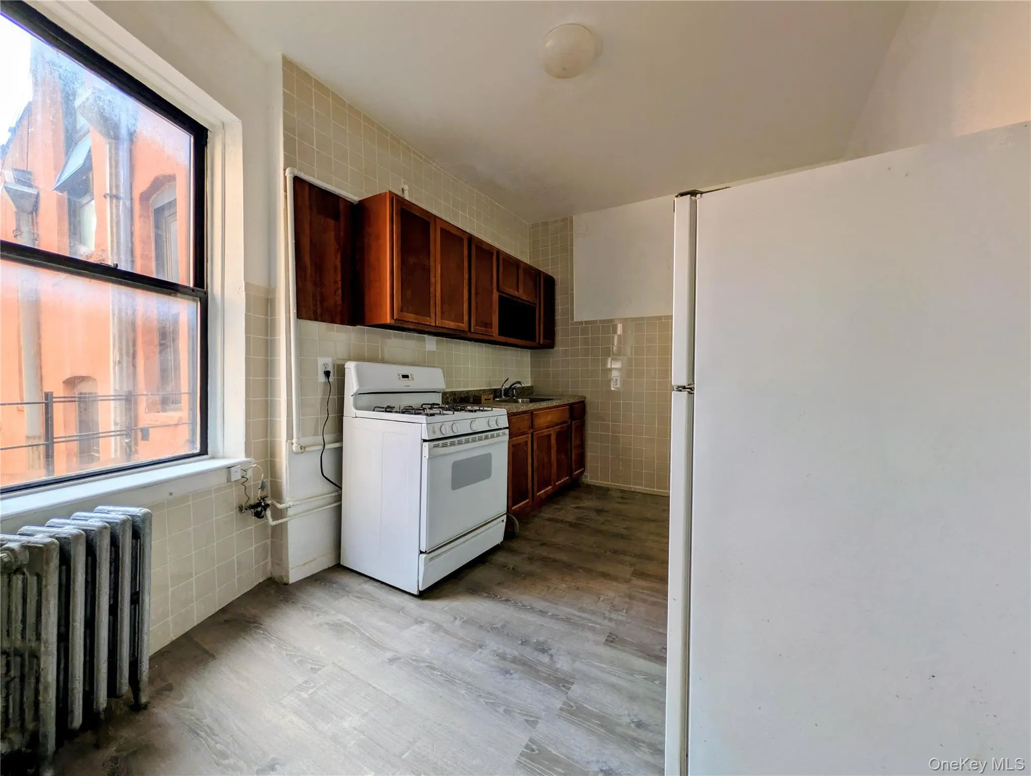 Kitchen with tile walls, white appliances, radiator heating unit, and light wood-style floors Kitchen with tile walls, white appliances, radiator heating unit, and light wood-style floors