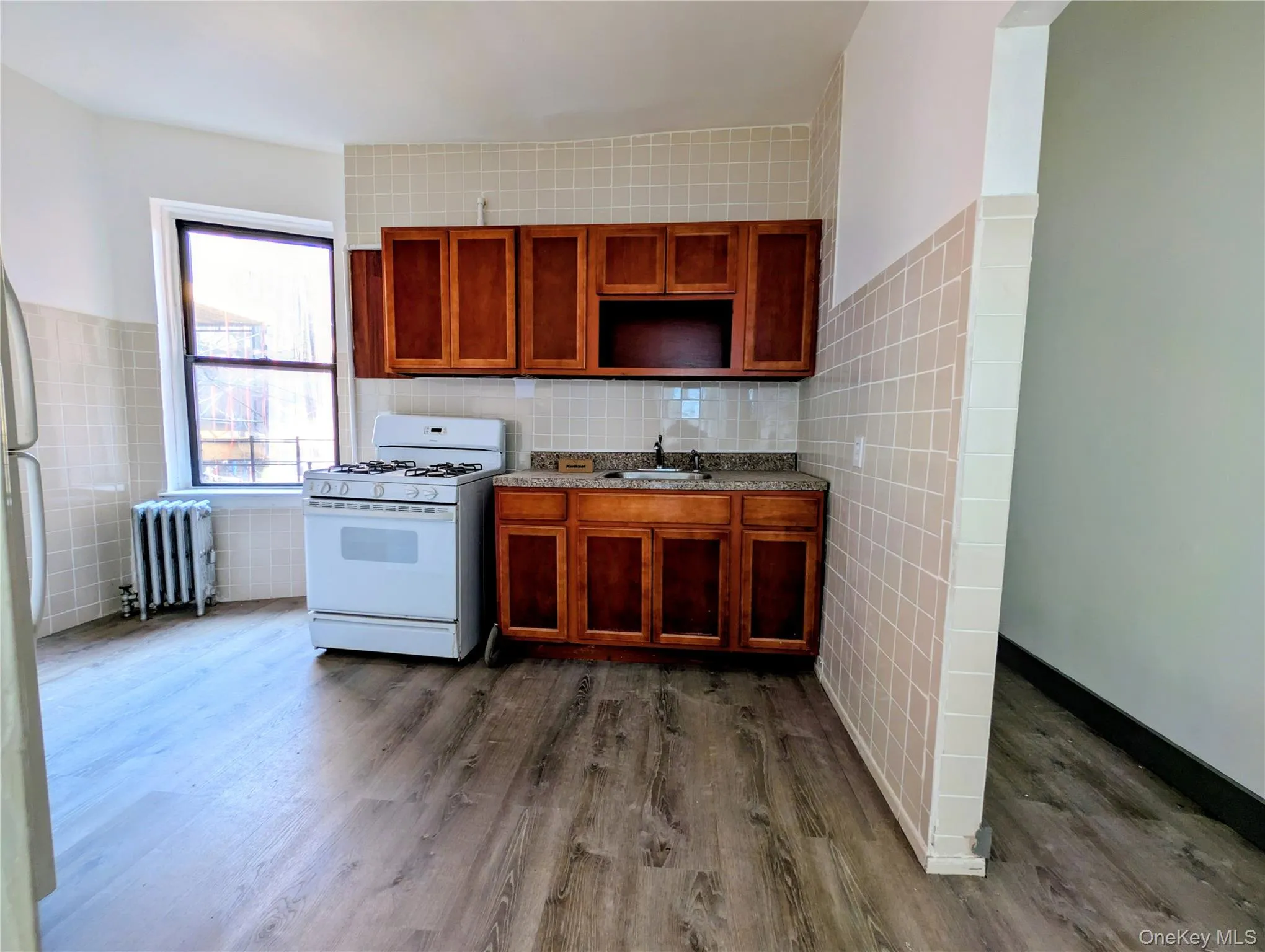 Kitchen featuring tile walls, white range with gas stovetop, brown cabinets, dark wood finished floors, and radiator heating unit Kitchen featuring tile walls, white range with gas stovetop, brown cabinets, dark wood finished floors, and radiator heating unit