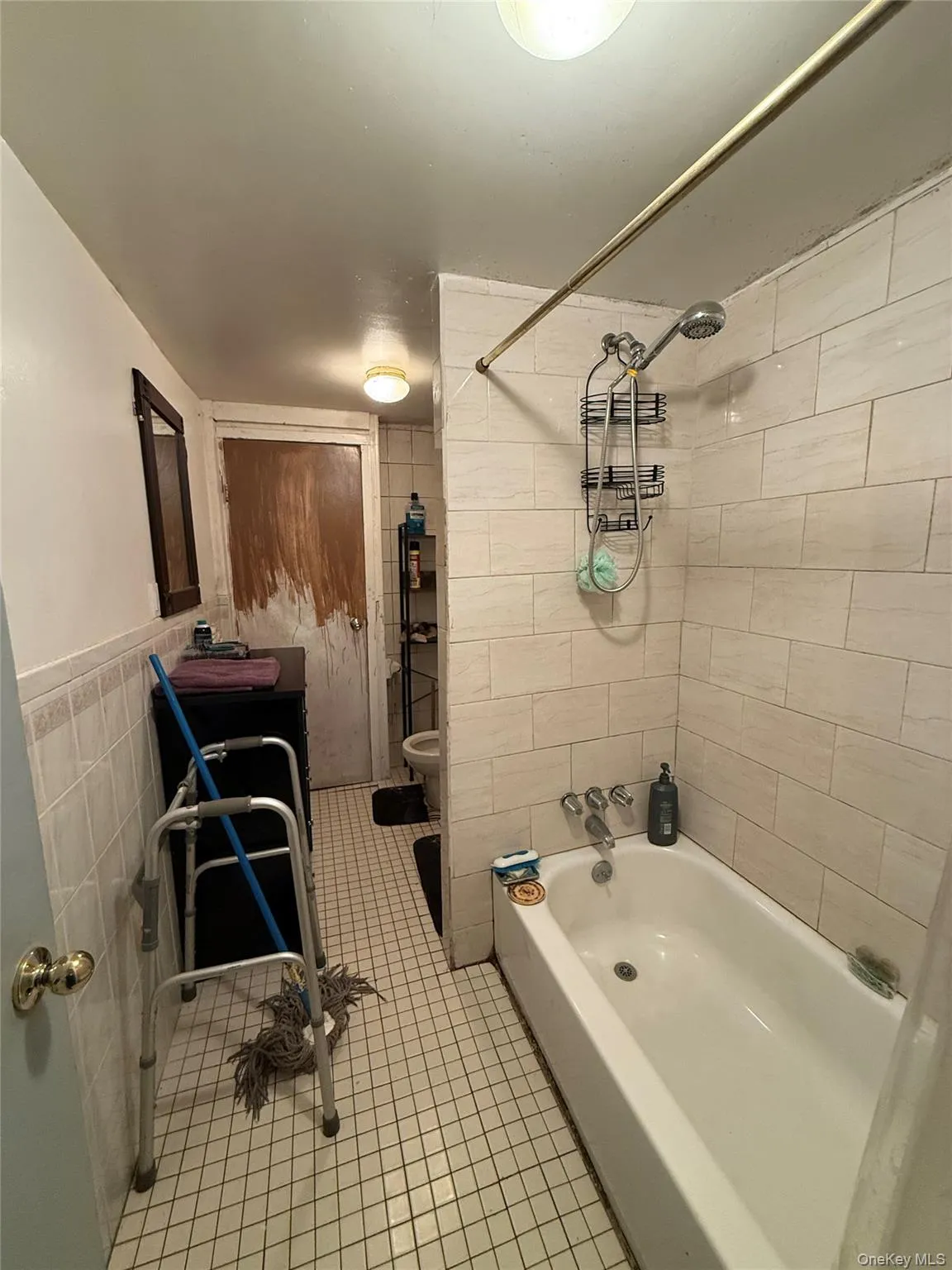 Full bathroom with tile walls, washtub / shower combination, and light tile patterned flooring Full bathroom with tile walls, washtub / shower combination, and light tile patterned flooring