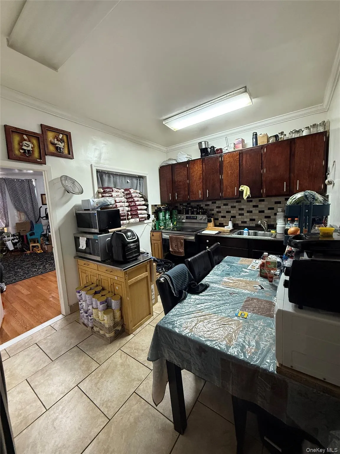 Kitchen featuring tasteful backsplash, crown molding, light tile patterned flooring, dark brown cabinetry, and stainless steel appliances Kitchen featuring tasteful backsplash, crown molding, light tile patterned flooring, dark brown cabinetry, and stainless steel appliances