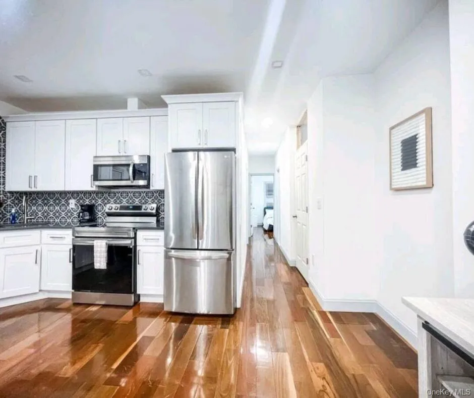 Kitchen with white cabinetry, tasteful backsplash, appliances with stainless steel finishes, dark wood-style flooring, and dark stone counters Kitchen with white cabinetry, tasteful backsplash, appliances with stainless steel finishes, dark wood-style flooring, and dark stone counters