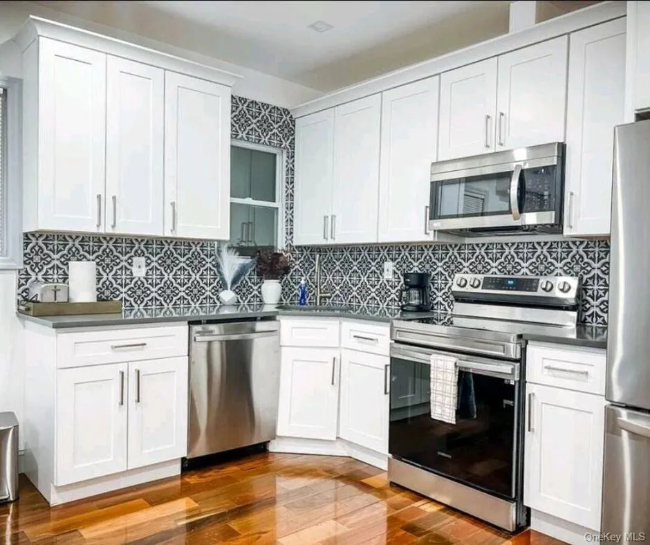 Kitchen featuring appliances with stainless steel finishes, white cabinets, dark wood-style floors, and decorative backsplash Kitchen featuring appliances with stainless steel finishes, white cabinets, dark wood-style floors, and decorative backsplash