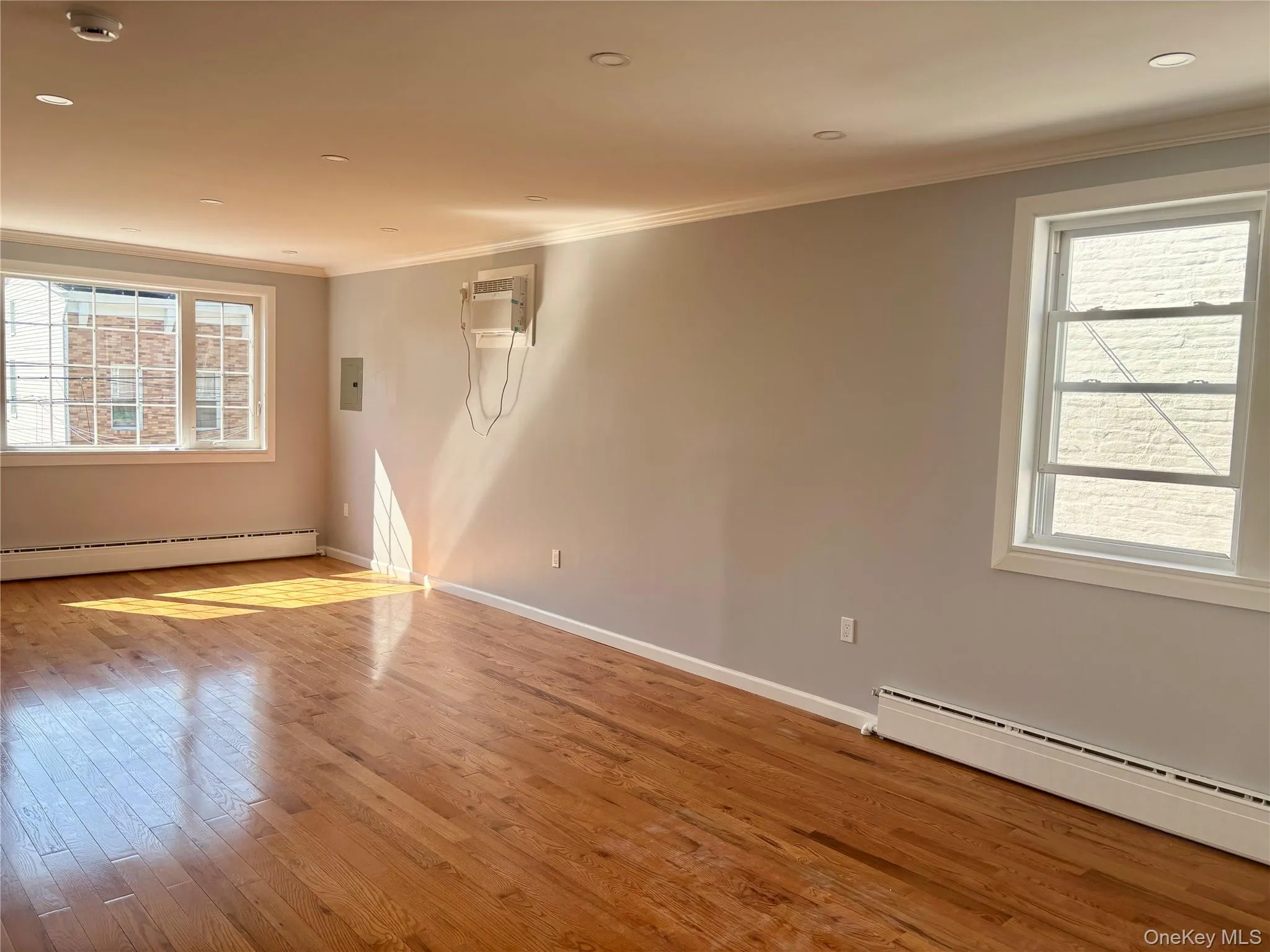 Unfurnished room with crown molding, light wood-style flooring, baseboard heating, recessed lighting, and a wall mounted AC Unfurnished room with crown molding, light wood-style flooring, baseboard heating, recessed lighting, and a wall mounted AC