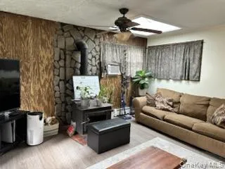 Living room with a wood stove, a ceiling fan, and wood finished floors Living room with a wood stove, a ceiling fan, and wood finished floors