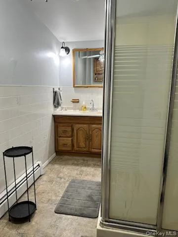 Full bathroom featuring a baseboard radiator, a stall shower, vanity, tile walls, and wainscoting Full bathroom featuring a baseboard radiator, a stall shower, vanity, tile walls, and wainscoting