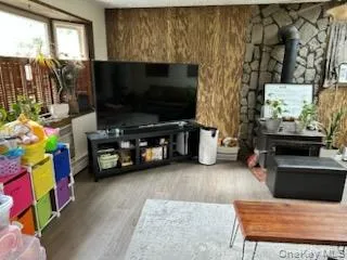 Living area featuring a wood stove, light wood-style flooring, a textured ceiling, and a baseboard radiator Living area featuring a wood stove, light wood-style flooring, a textured ceiling, and a baseboard radiator