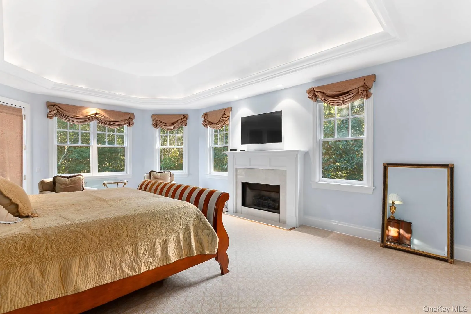 Bedroom featuring a fireplace, carpet floors, and a raised ceiling Bedroom featuring a fireplace, carpet floors, and a raised ceiling