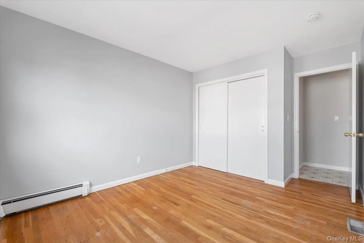 Unfurnished bedroom featuring a baseboard radiator, light wood-style flooring, and a closet Unfurnished bedroom featuring a baseboard radiator, light wood-style flooring, and a closet
