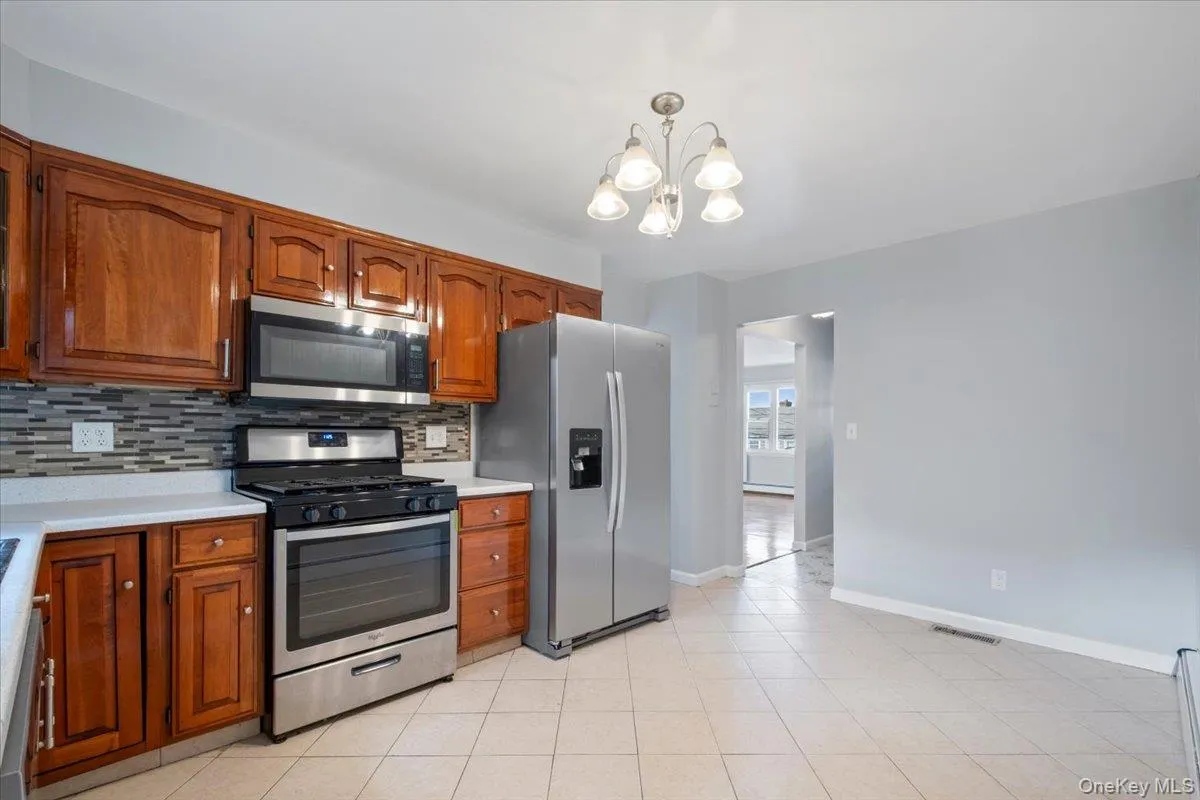 Kitchen with appliances with stainless steel finishes, brown cabinetry, tasteful backsplash, and a chandelier Kitchen with appliances with stainless steel finishes, brown cabinetry, tasteful backsplash, and a chandelier