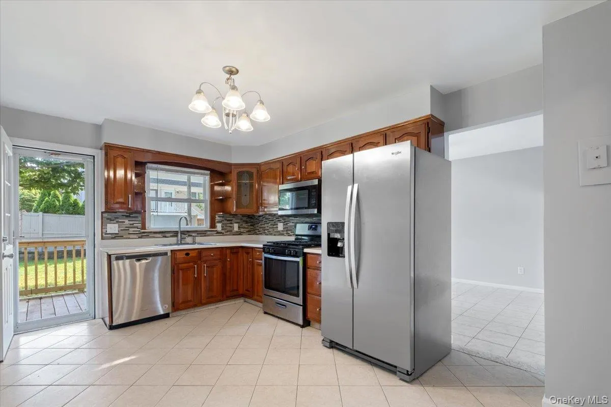 Kitchen with appliances with stainless steel finishes, light countertops, tasteful backsplash, light tile patterned floors, and brown cabinetry Kitchen with appliances with stainless steel finishes, light countertops, tasteful backsplash, light tile patterned floors, and brown cabinetry