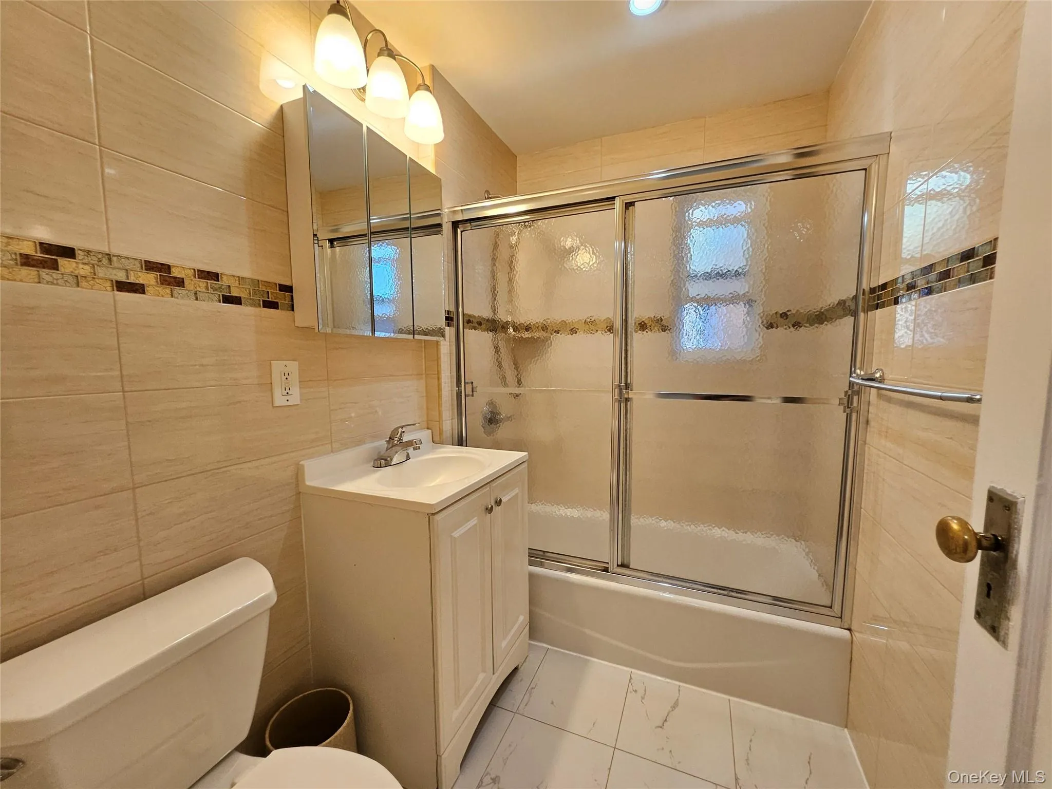 Full bathroom featuring tile walls, combined bath / shower with glass door, vanity, and light marble finish floors Full bathroom featuring tile walls, combined bath / shower with glass door, vanity, and light marble finish floors