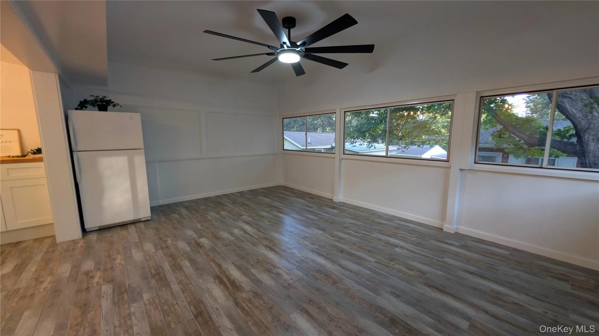 Unfurnished living room with dark wood-style flooring, ceiling fan, and a decorative wall Unfurnished living room with dark wood-style flooring, ceiling fan, and a decorative wall