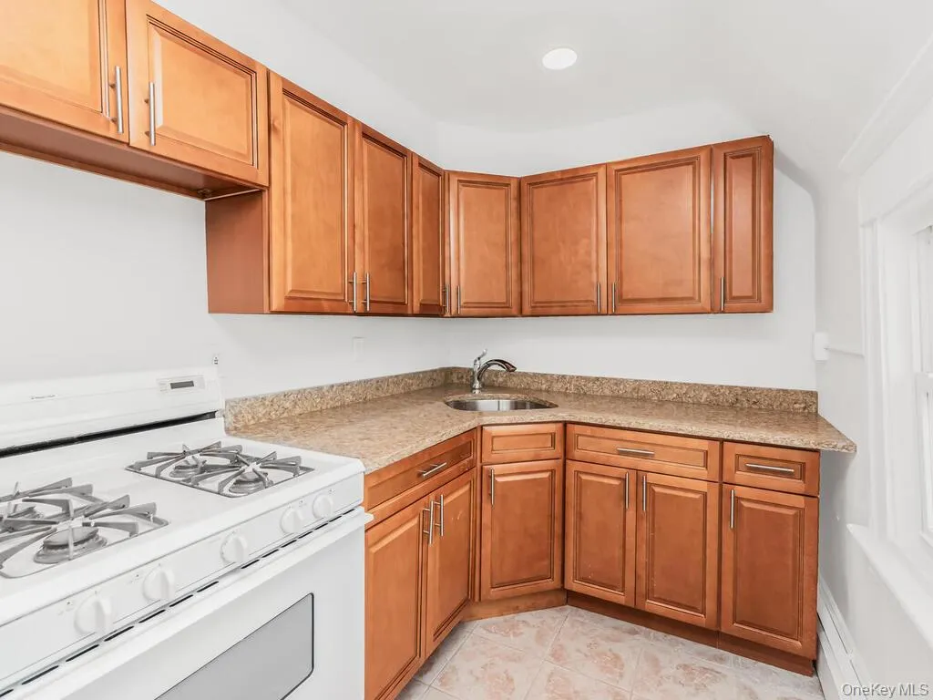 Kitchen featuring white gas range, brown cabinets, light stone countertops, light tile patterned floors, and recessed lighting Kitchen featuring white gas range, brown cabinets, light stone countertops, light tile patterned floors, and recessed lighting